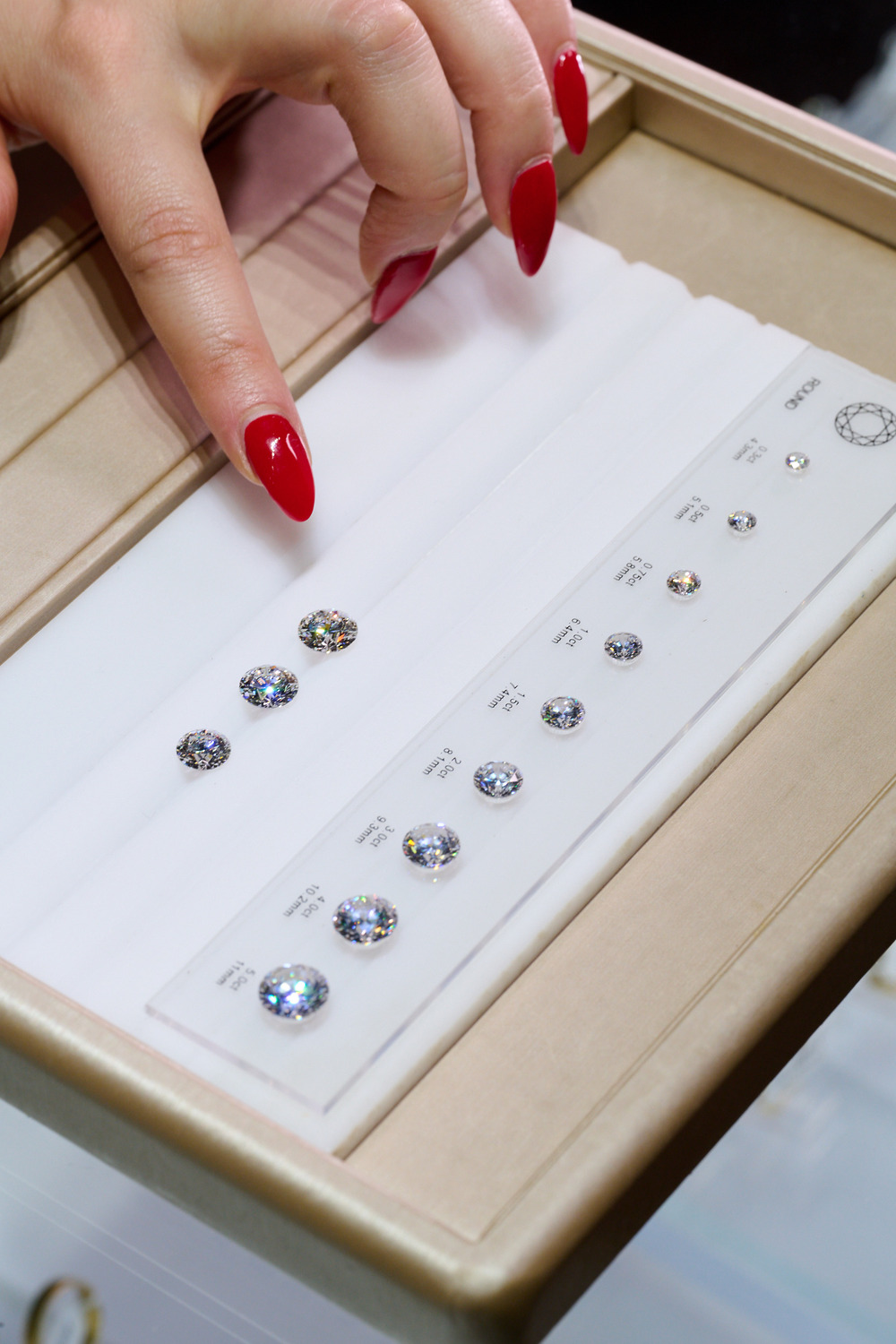 A hand with red nails points at round cut diamonds in a jewelry tray, perfect for a destination wedding.