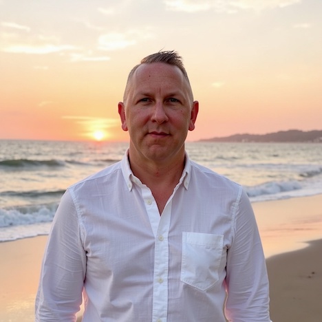 A man in a white shirt stands on the beach at sunset, waves rolling behind him at a destination wedding.