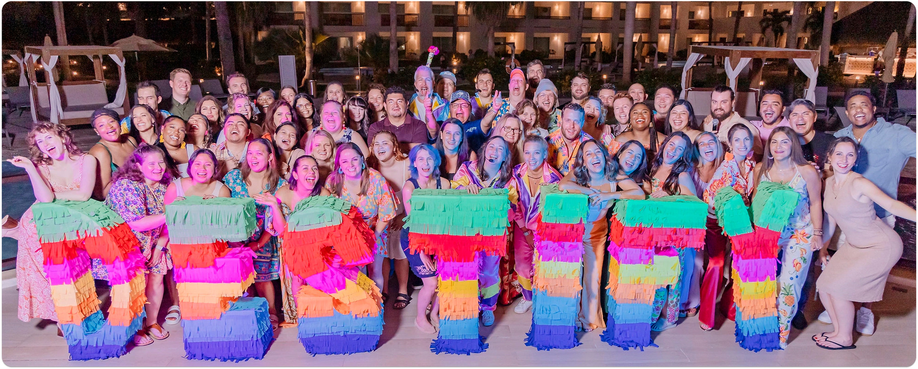 At a destination wedding, a joyful group poses at night holding colorful letters spelling "RETREAT.
