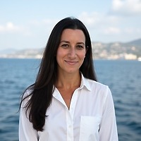 Woman in a white shirt standing outdoors by the water, evoking a serene destination wedding setting.