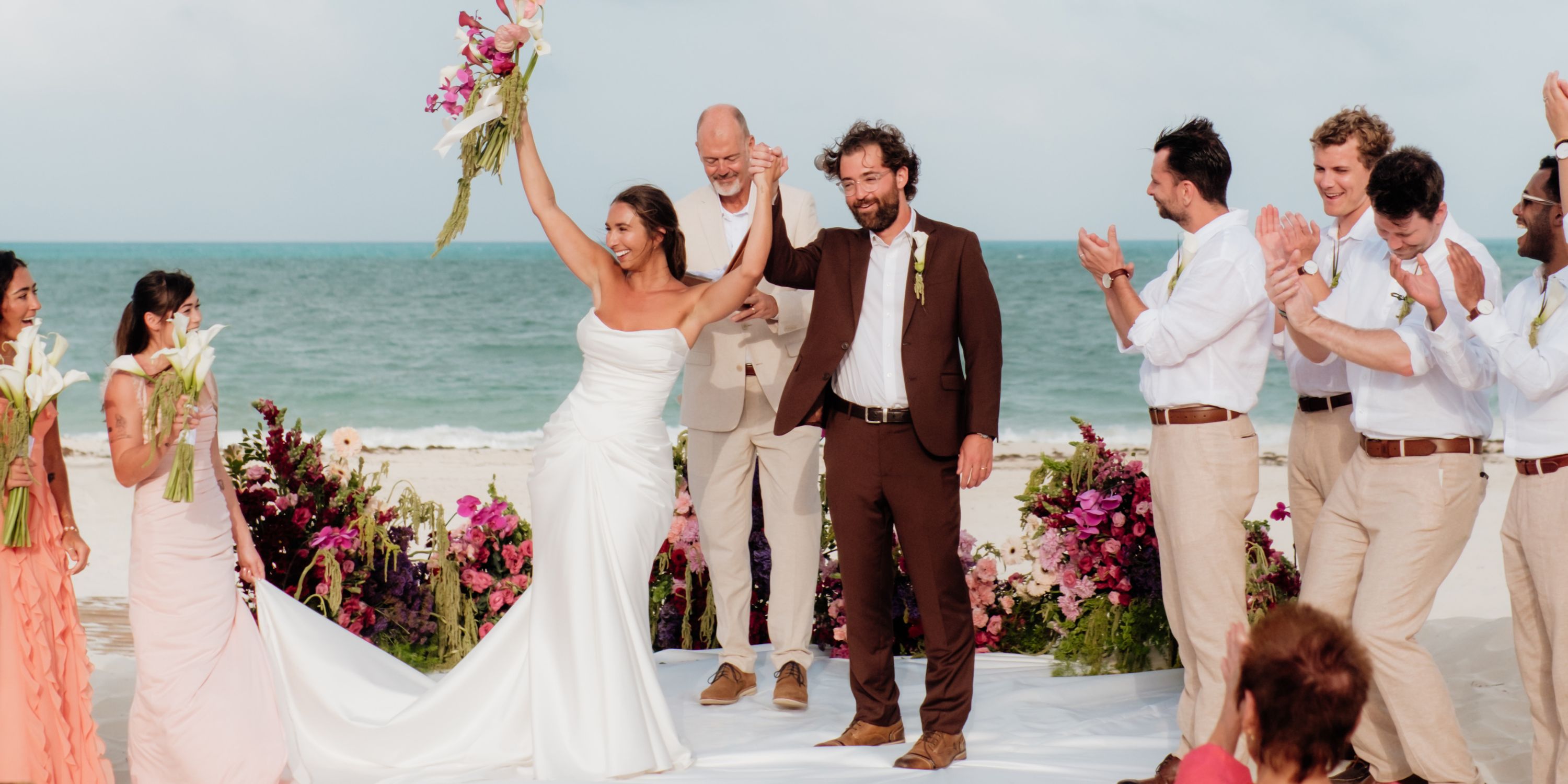 Ethan and Erica enjoy their destination wedding on the beach, joined by guests cheering around them.