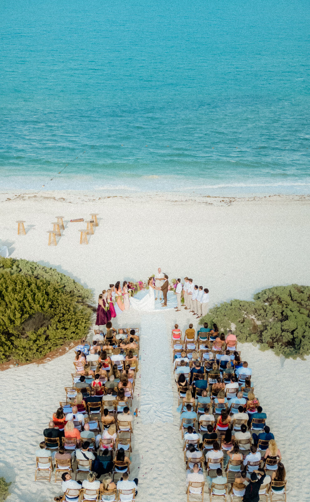 Wedding guests sit facing Ethan and Erica with the officiant at a destination wedding by the shore.