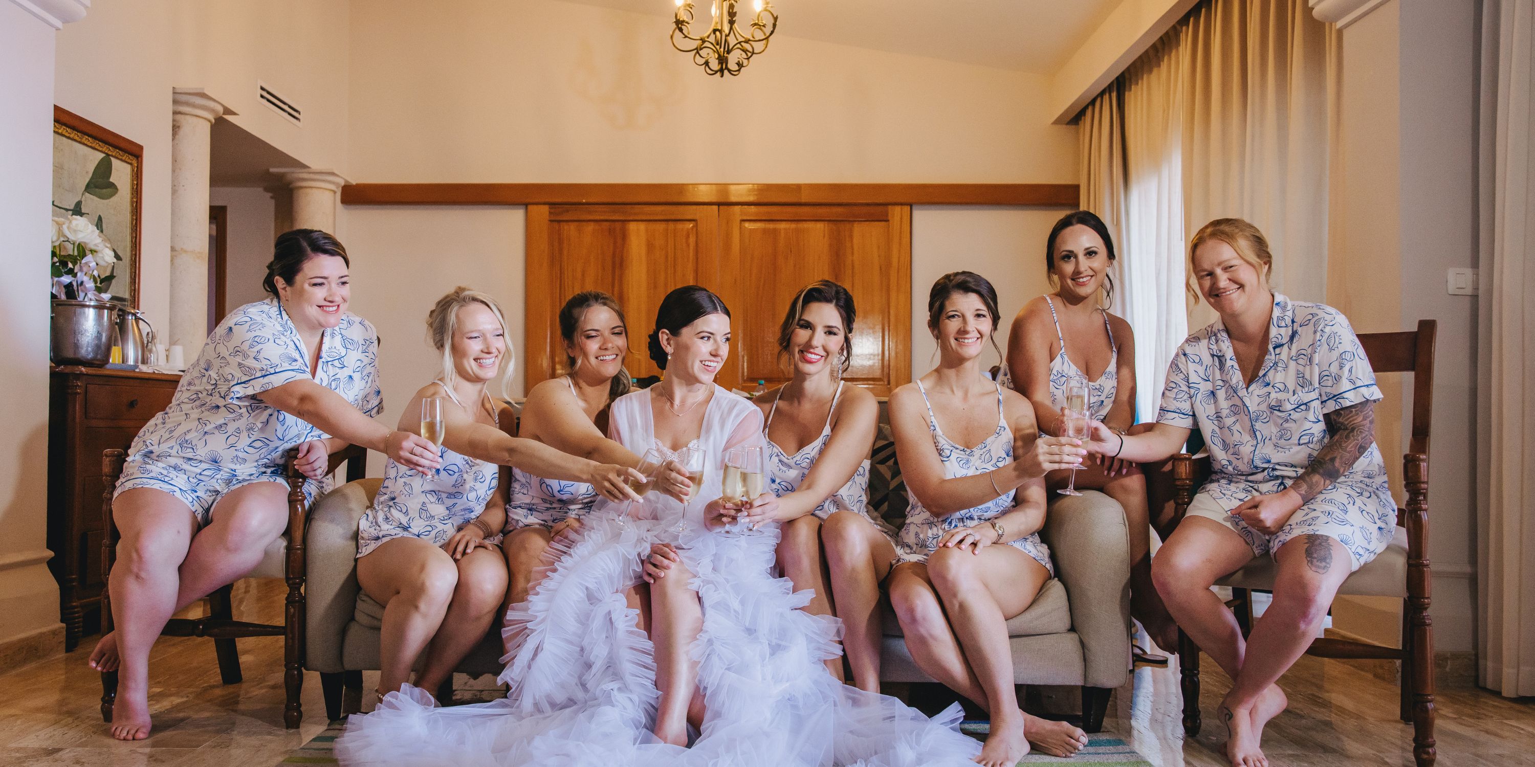 Bride and bridesmaids in matching pajamas toasting in a living room before the destination wedding.