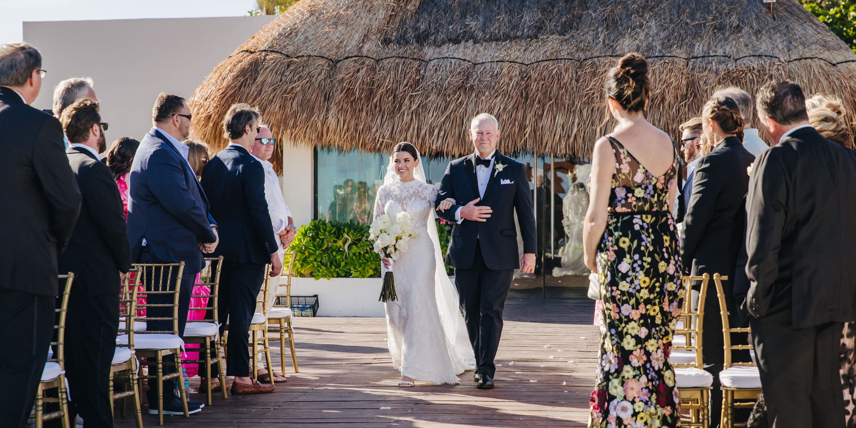 Kathryn in a white dress walks down the outdoor aisle at a destination wedding, guests on both sides.