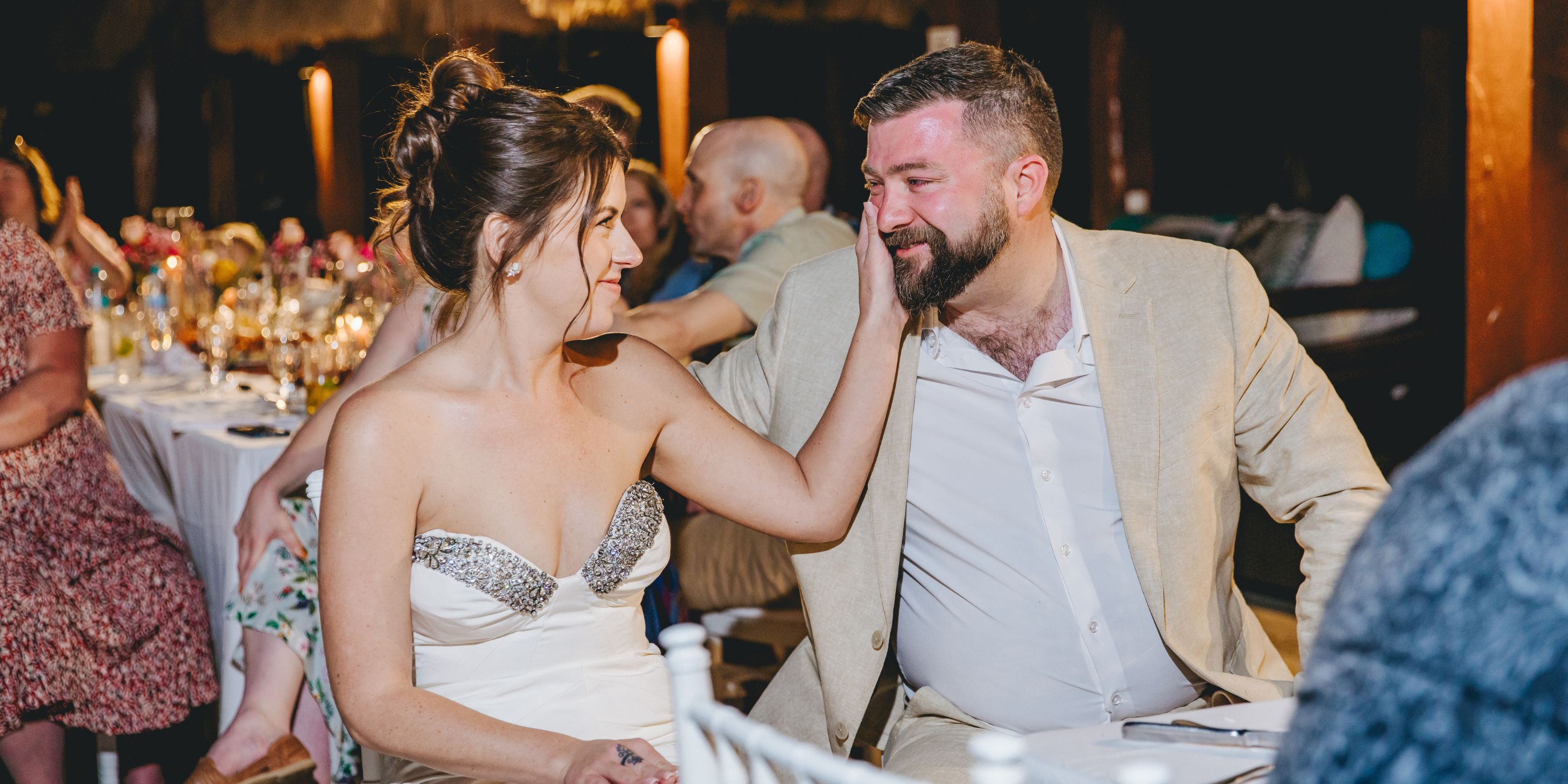 Kathryn, in a strapless dress, touches Mike's face as they smile at a destination wedding with guests.