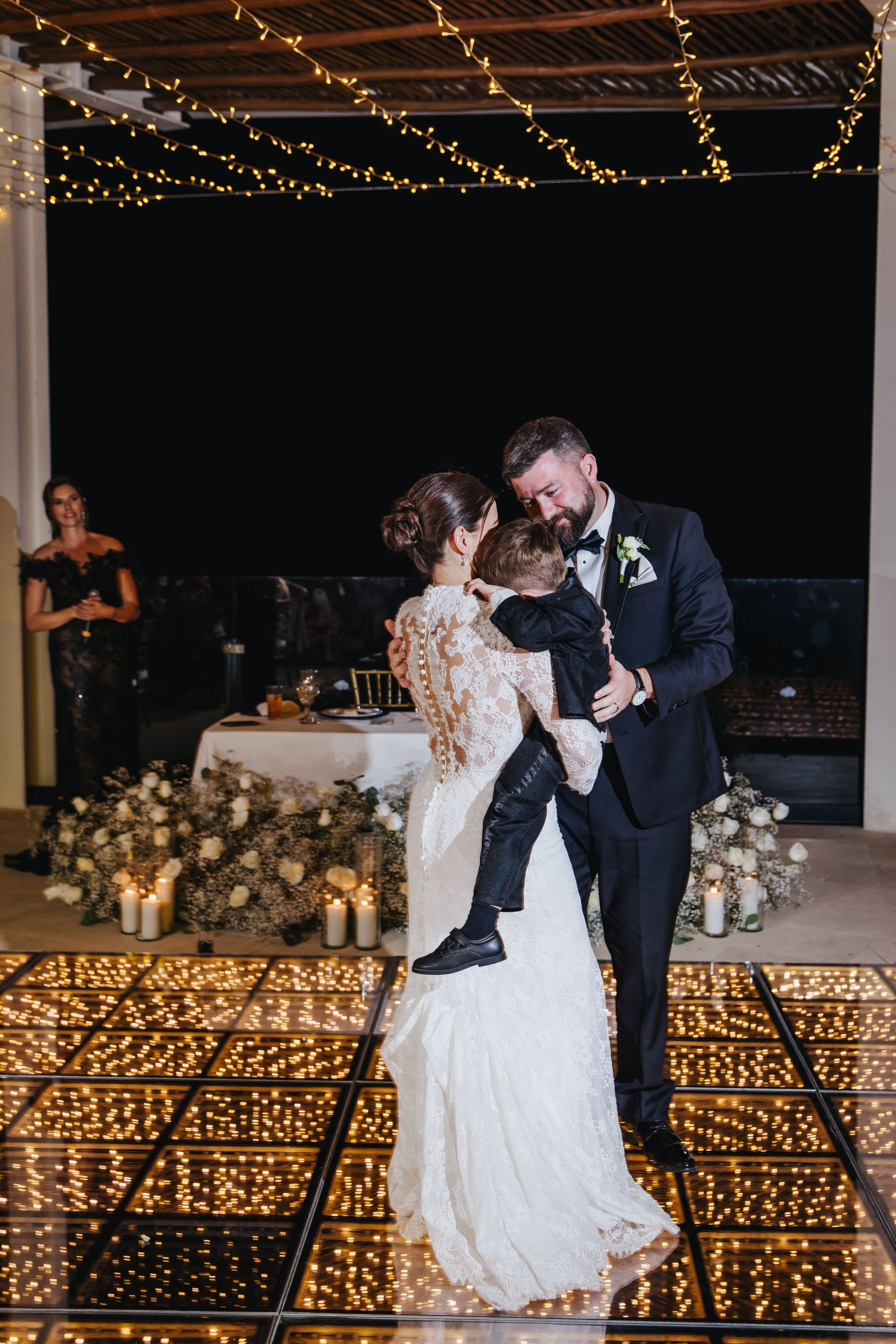 Kathryn and Mike dance with a young boy on a glowing floor at their destination wedding, flowers and candles around.