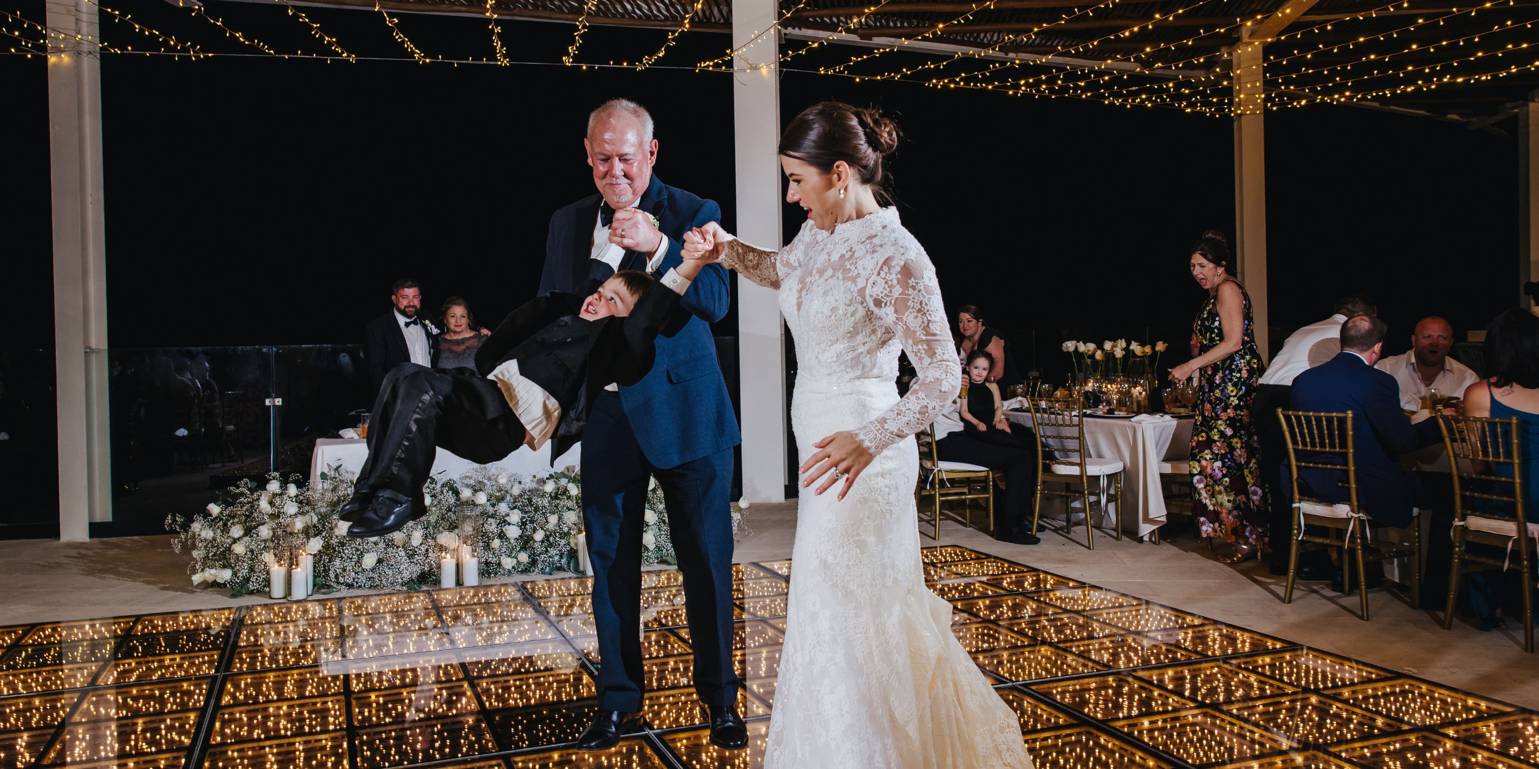 Kathryn and Mike swing a child on a glowing dance floor during their destination wedding reception.