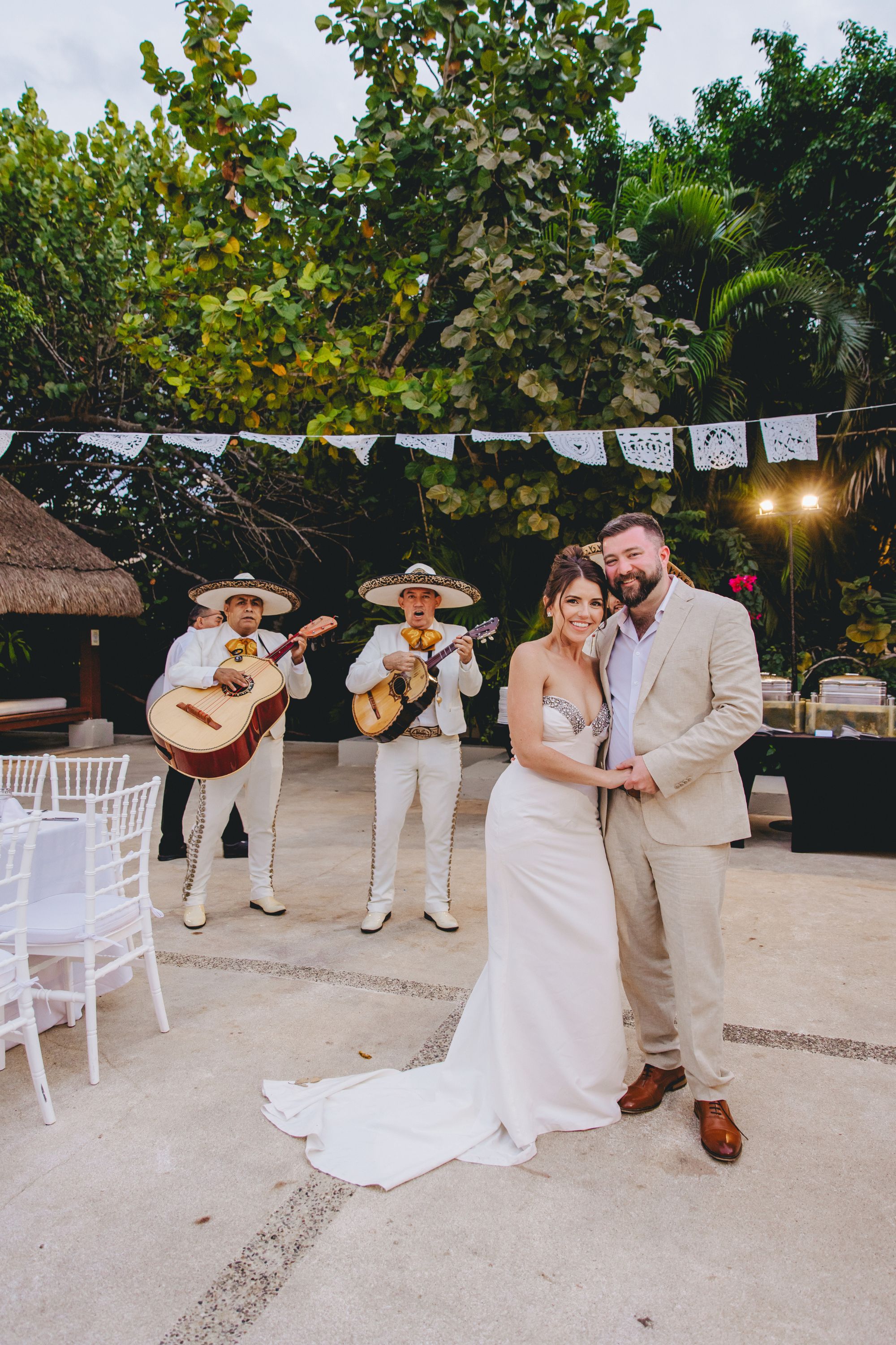 Kathryn and Mike pose outdoors at their destination wedding with a mariachi band playing behind them.