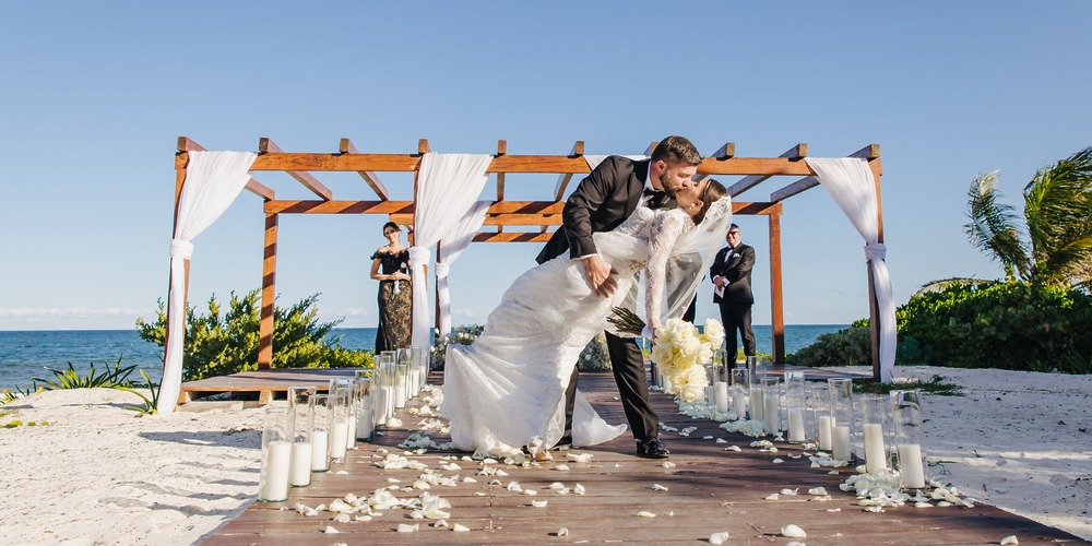 Kathryn and Mike share a kiss under a pergola on a beachside aisle during their destination wedding.