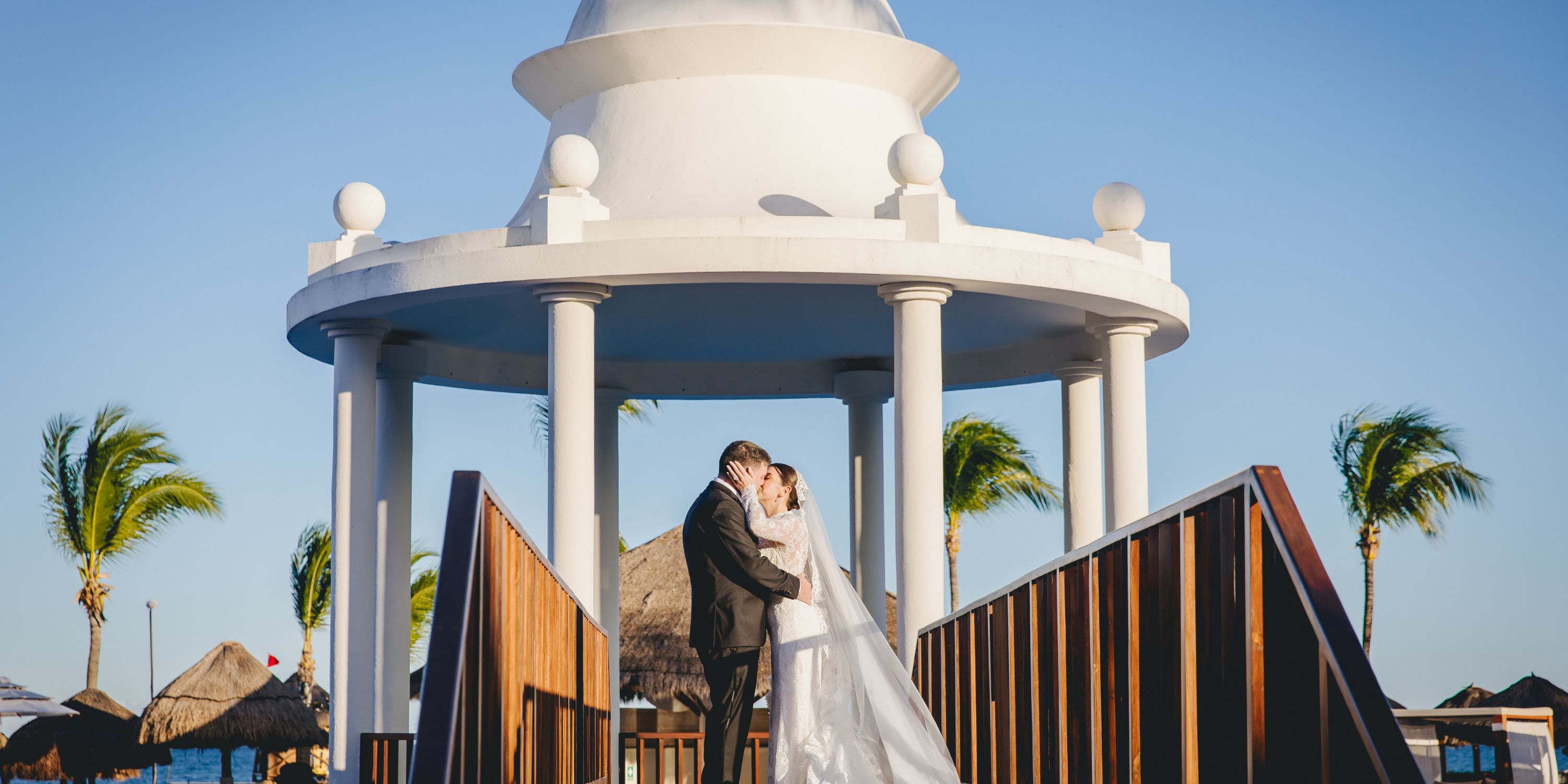Kathryn and Mike share a kiss at their destination wedding under a white gazebo with palm trees.