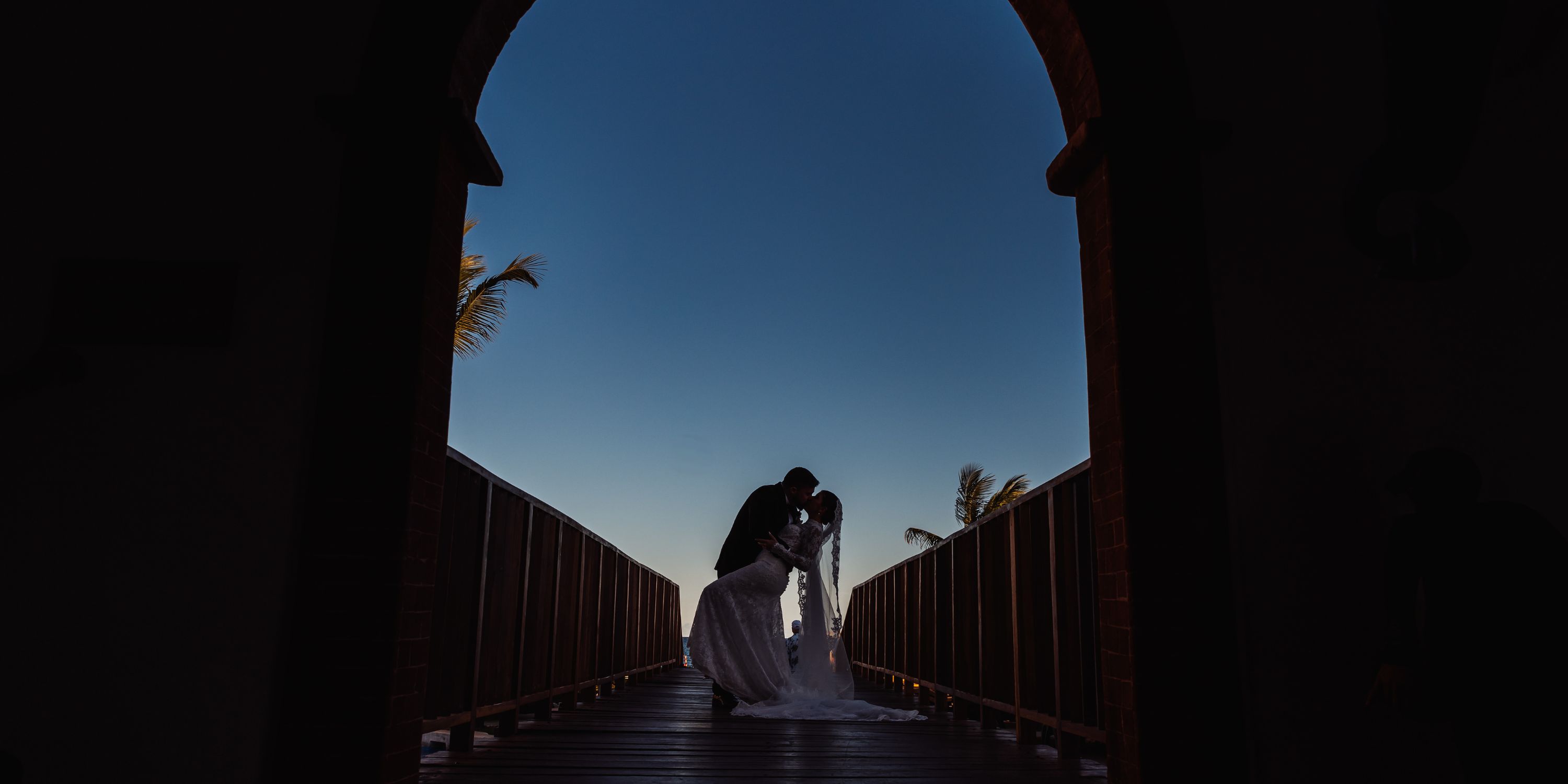 Kathryn and Mike share a kiss on a bridge at sunset during their destination wedding.