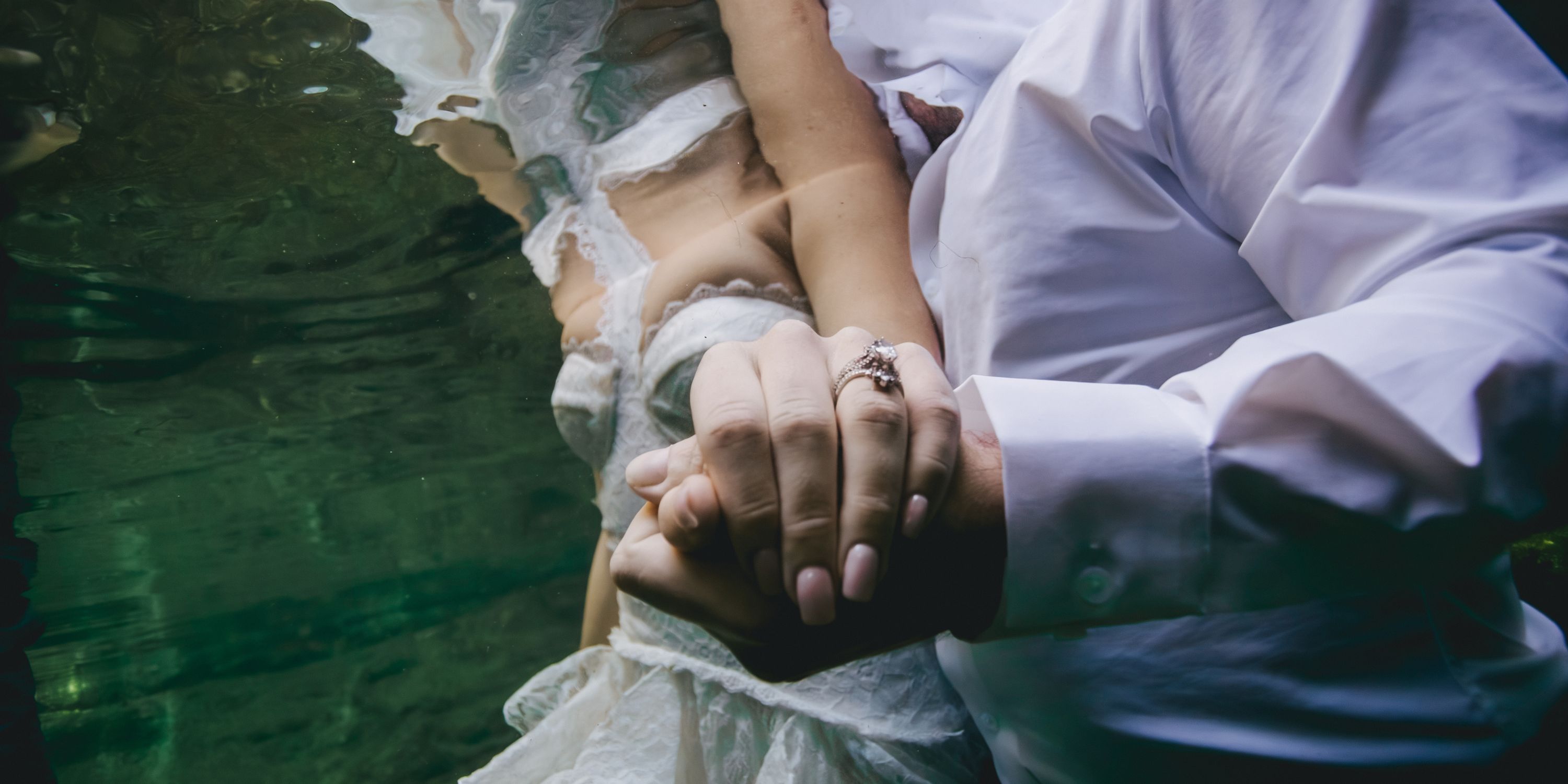 Two people in wedding attire hold hands underwater, with a ring highlighted&mdash;perfect destination wedding.