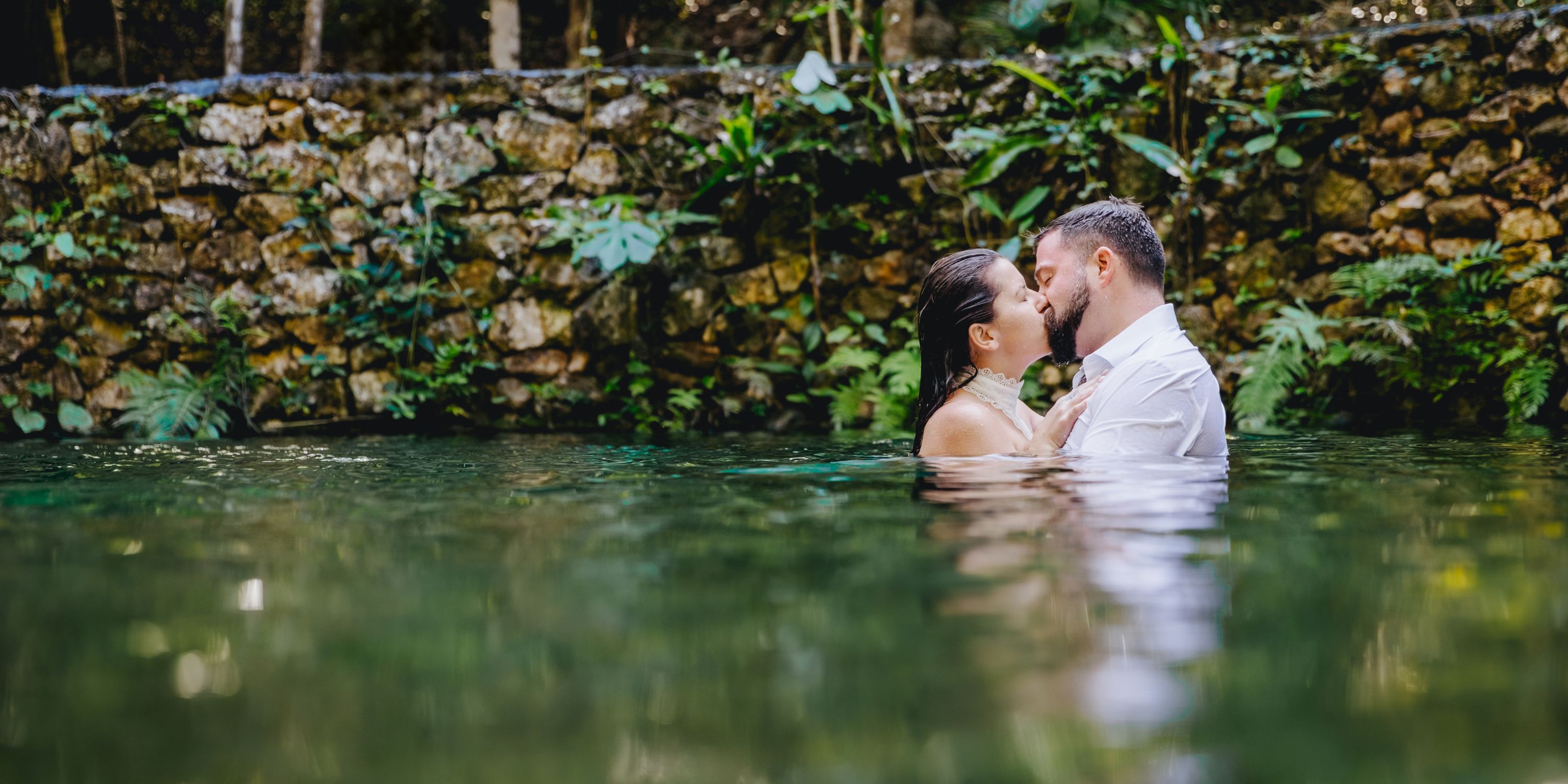 Kathryn and Mike share a kiss in a natural pool, stone wall behind them at their destination wedding.