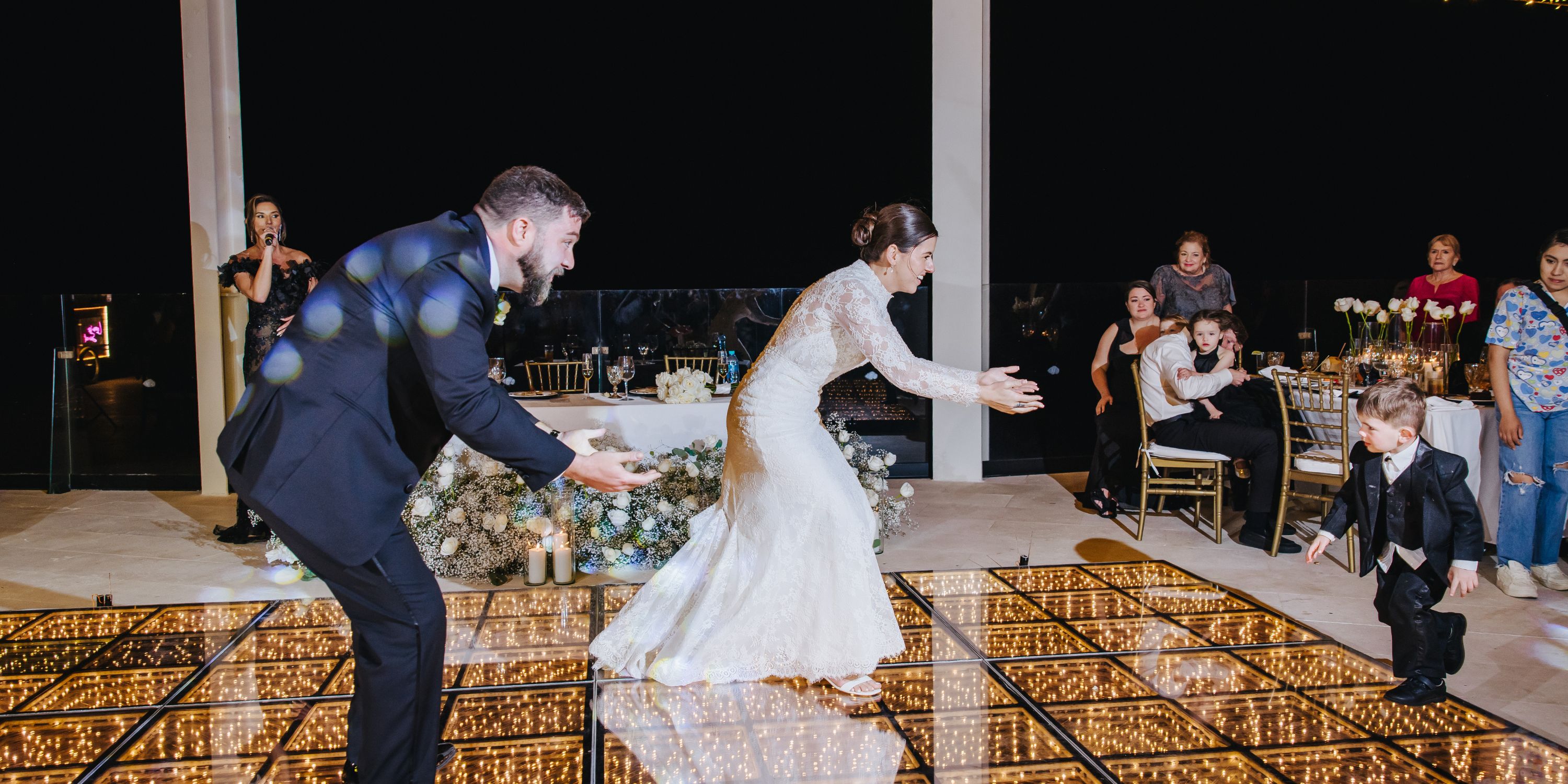 At a destination wedding, Kathryn and Mike reach for a young boy on the glowing dance floor as guests watch.