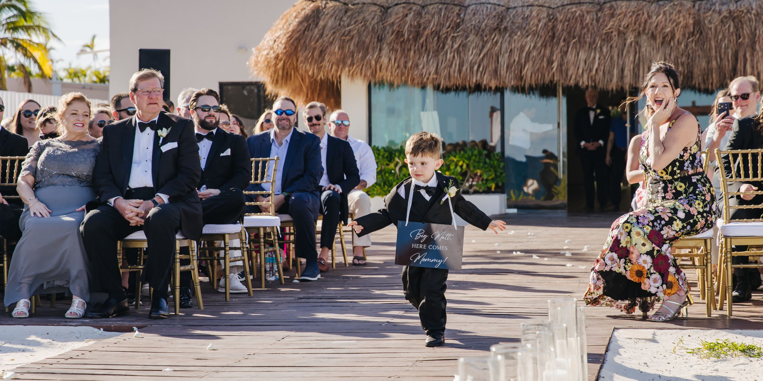 At the wedding, a young boy carries a "Here Comes Mommy" sign as he walks down the aisle.