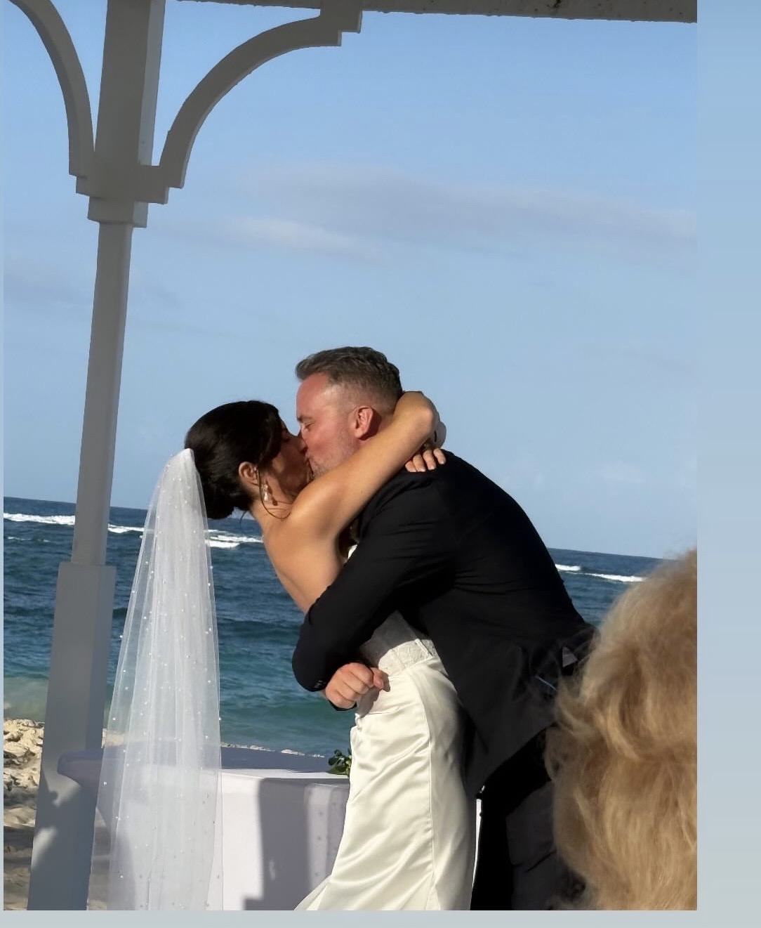 Hannah and Ben kiss during their romantic destination wedding ceremony on the beach.