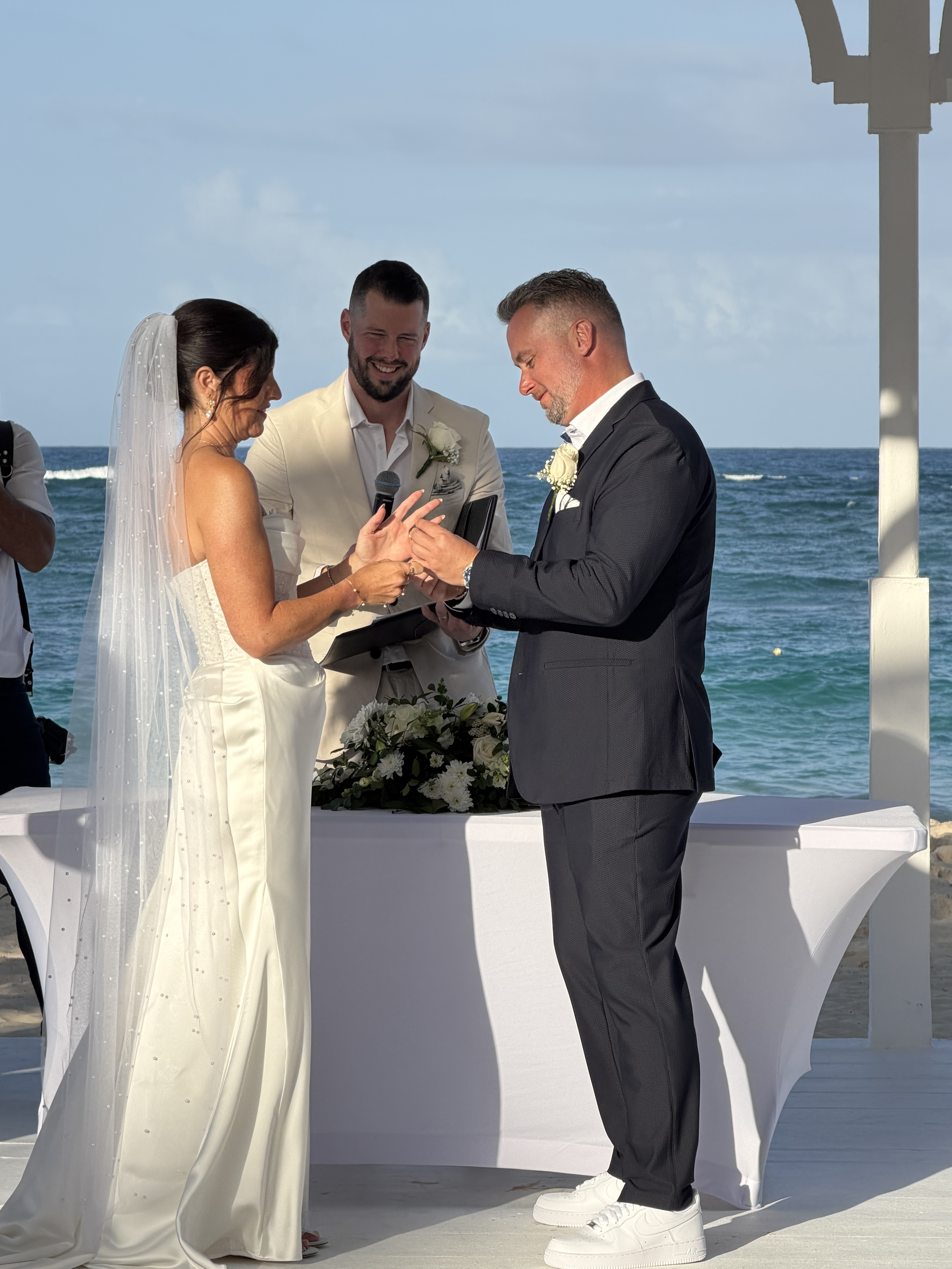 Hannah and Ben exchange rings during their destination wedding ceremony on a scenic outdoor beach.