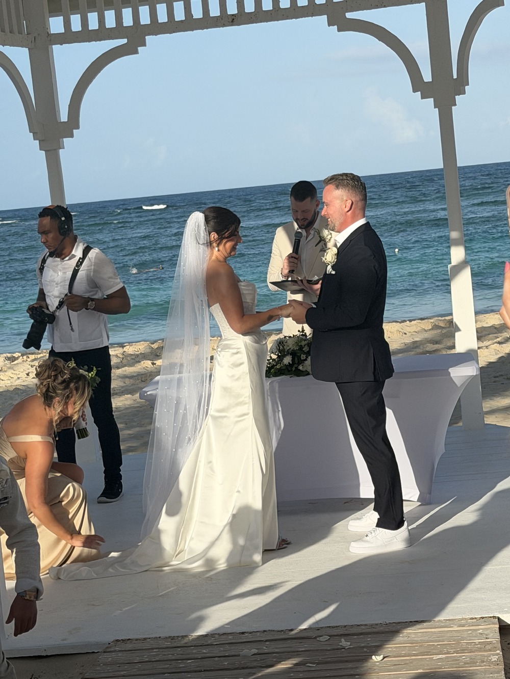 Hannah and Ben exchange rings during a destination wedding on the beach beneath a white gazebo.