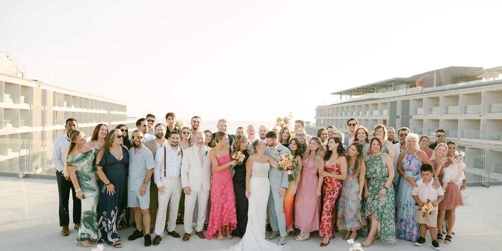 A large group gathers outdoors at Lauren and Ben&rsquo;s destination wedding, city buildings behind them.