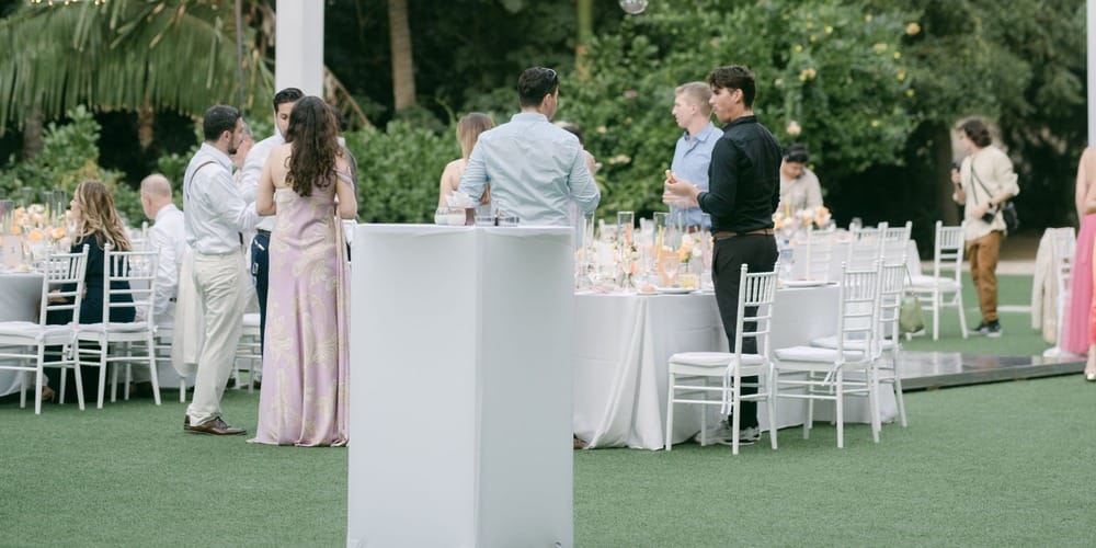 Guests socializing outdoors at a destination wedding at Lauren and Ben, with white tables on green grass.