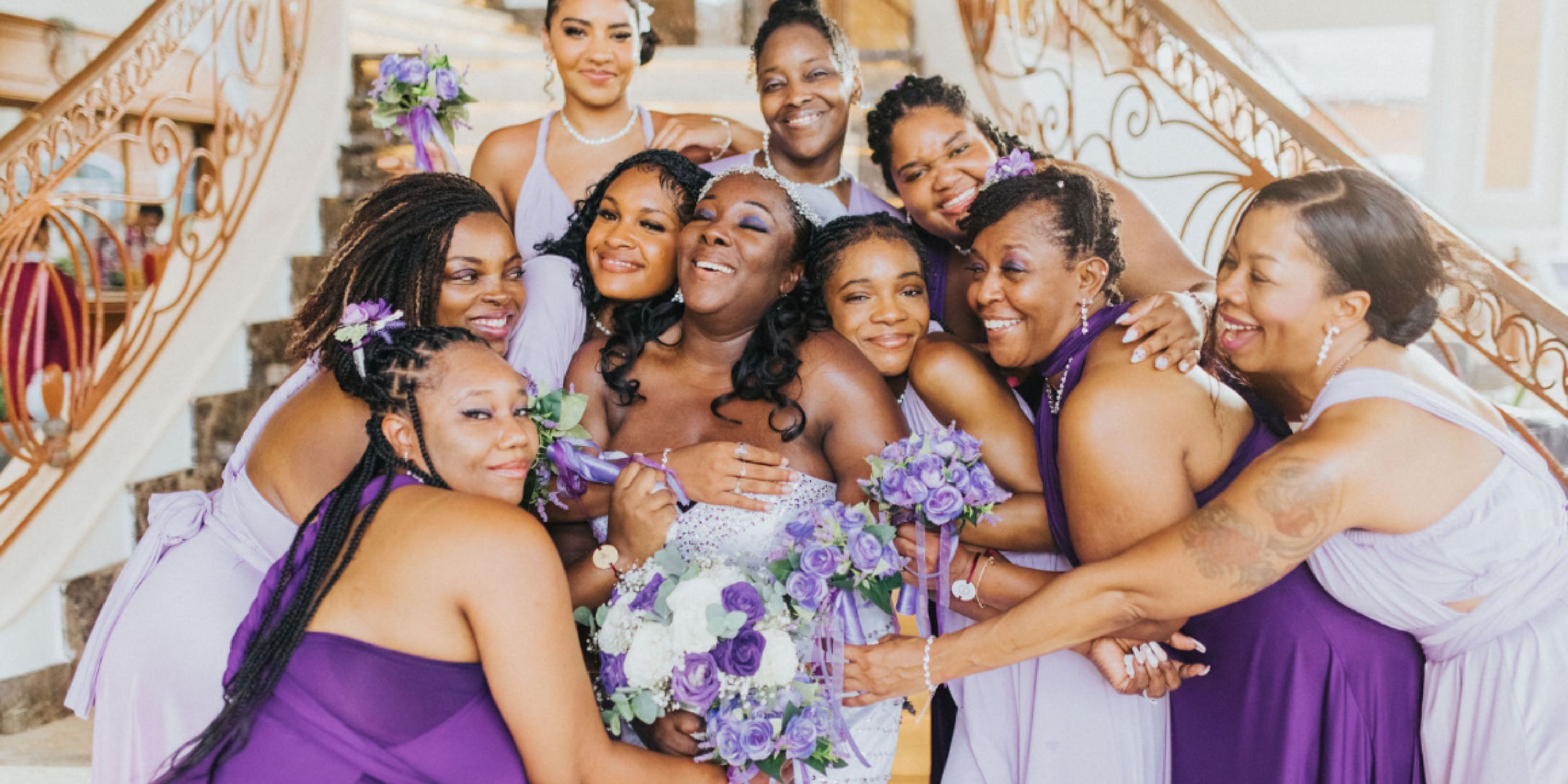 At a destination wedding, bridesmaids in purple hug the bride on a staircase.