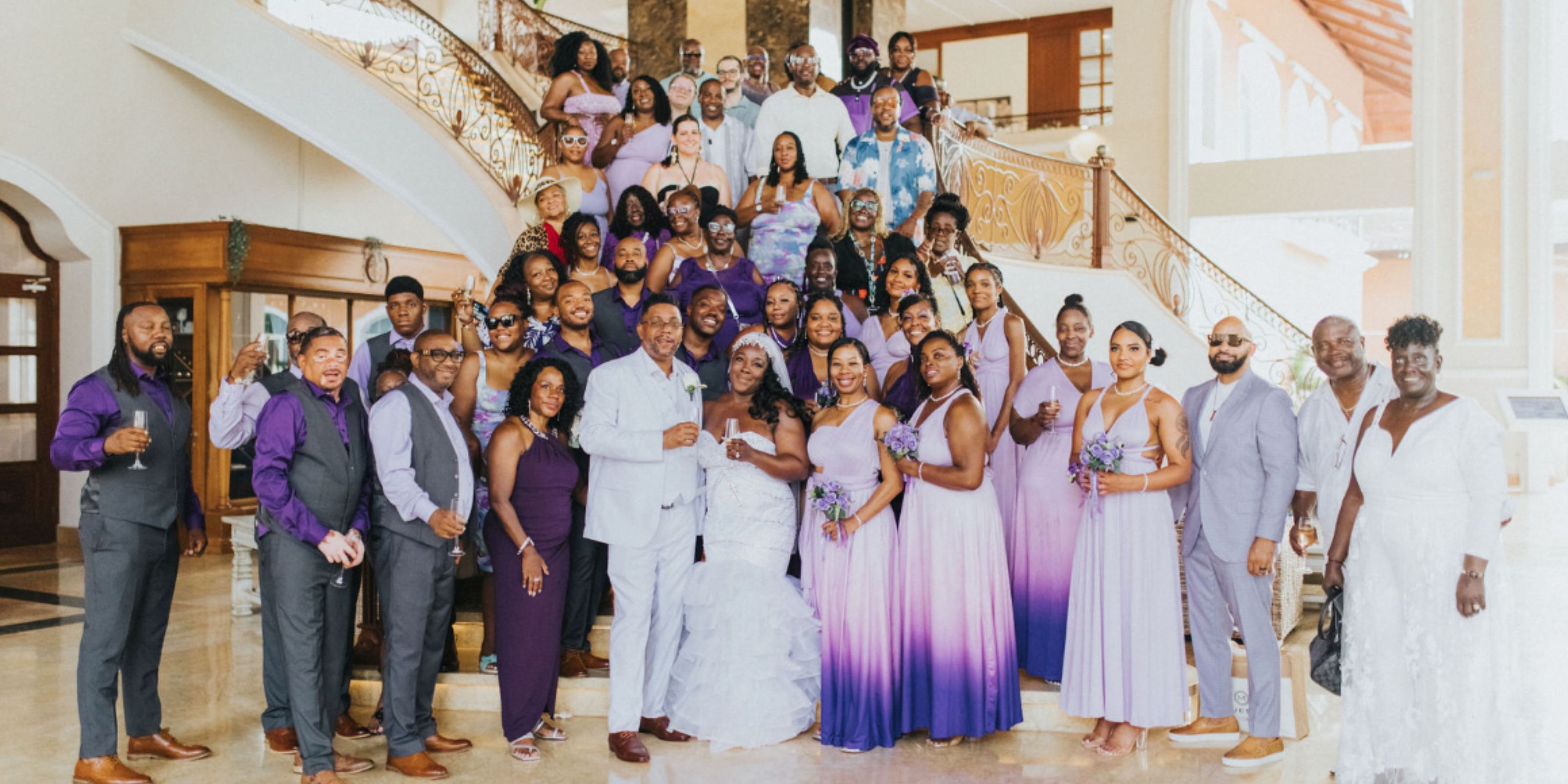 The Ethan and Erica (Copy) group poses on an indoor staircase in purple and white destination wedding attire.
