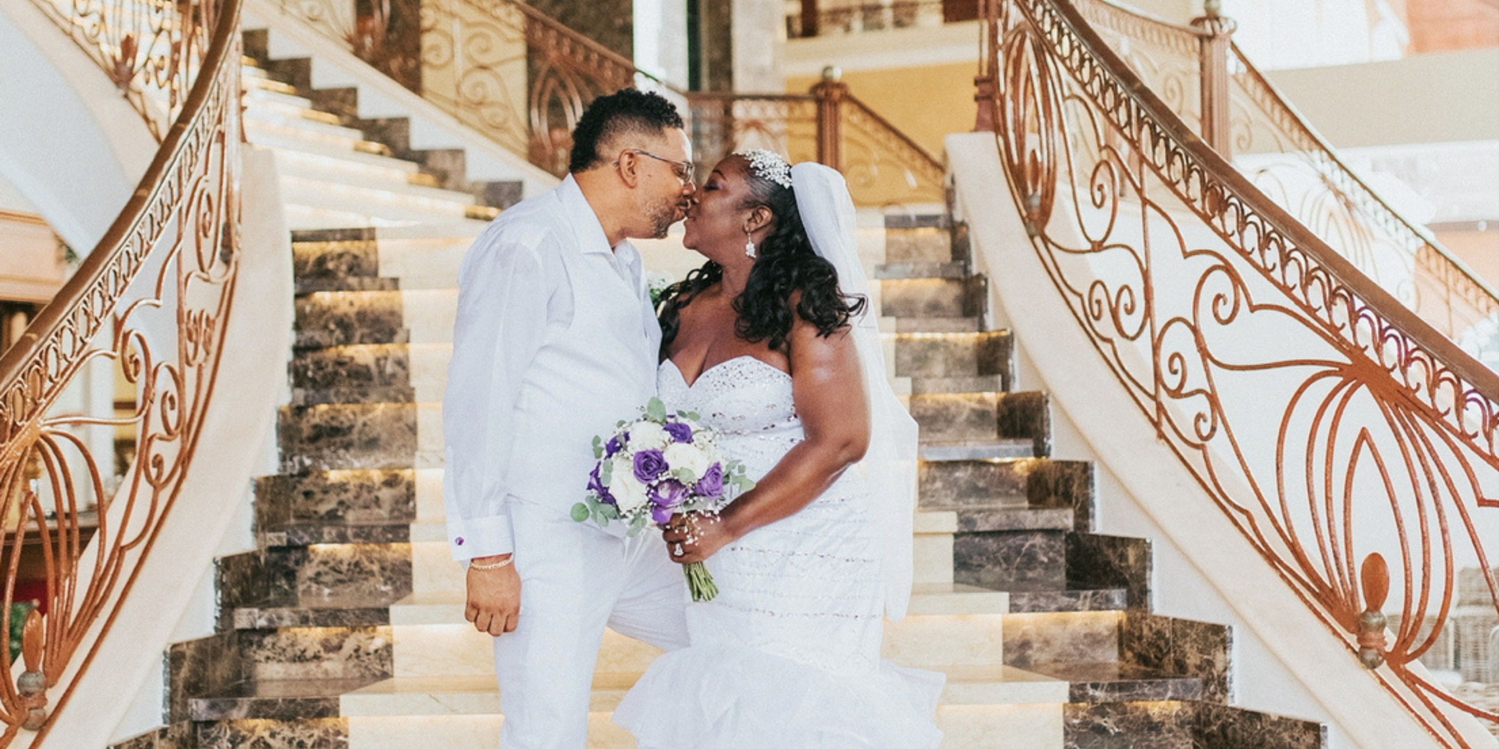 Bride and groom share a kiss on the staircase at their wedding, holding a purple bouquet.