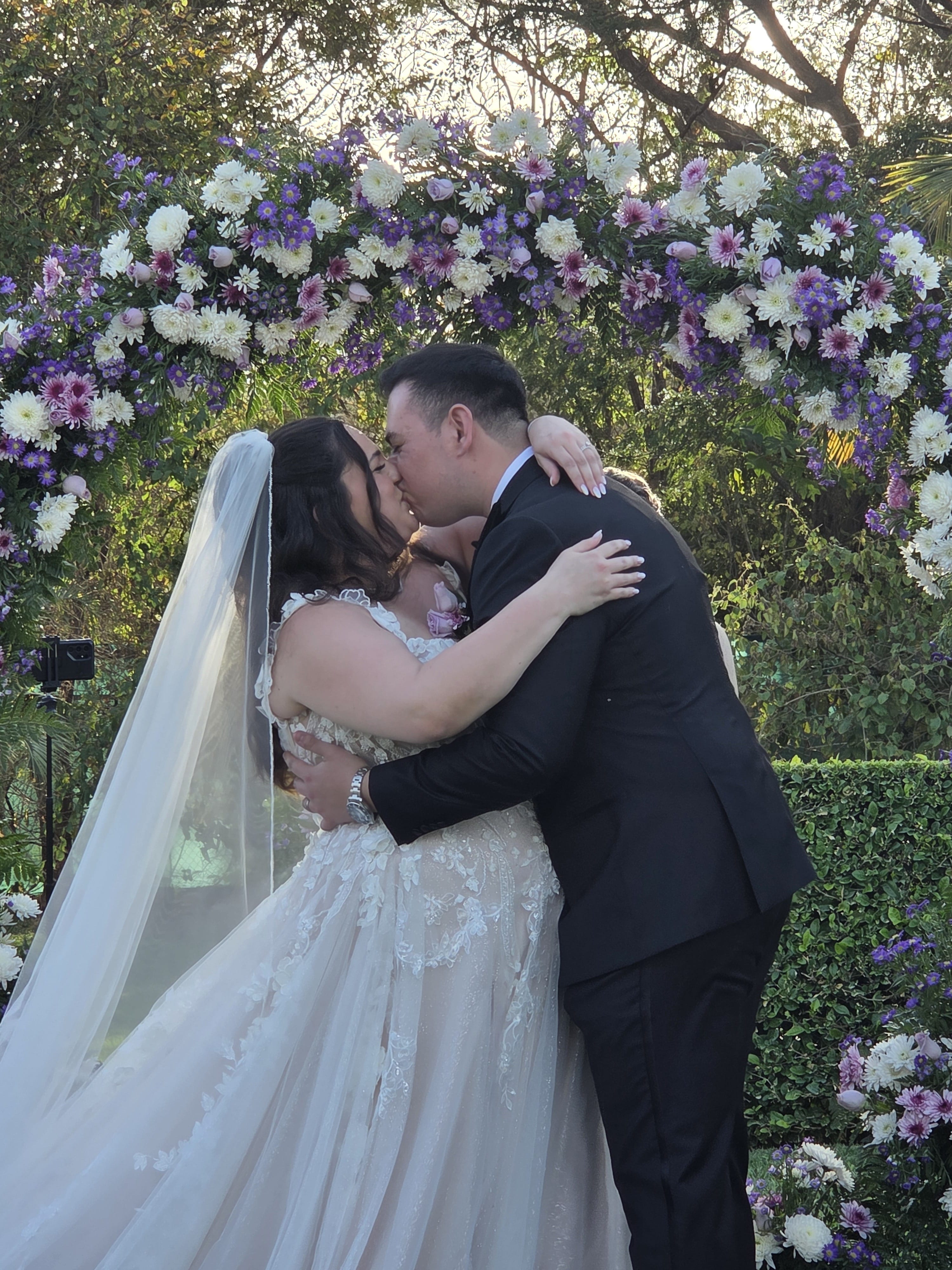 Ashley and Zach kiss beneath a floral arch during their romantic outdoor destination wedding ceremony.