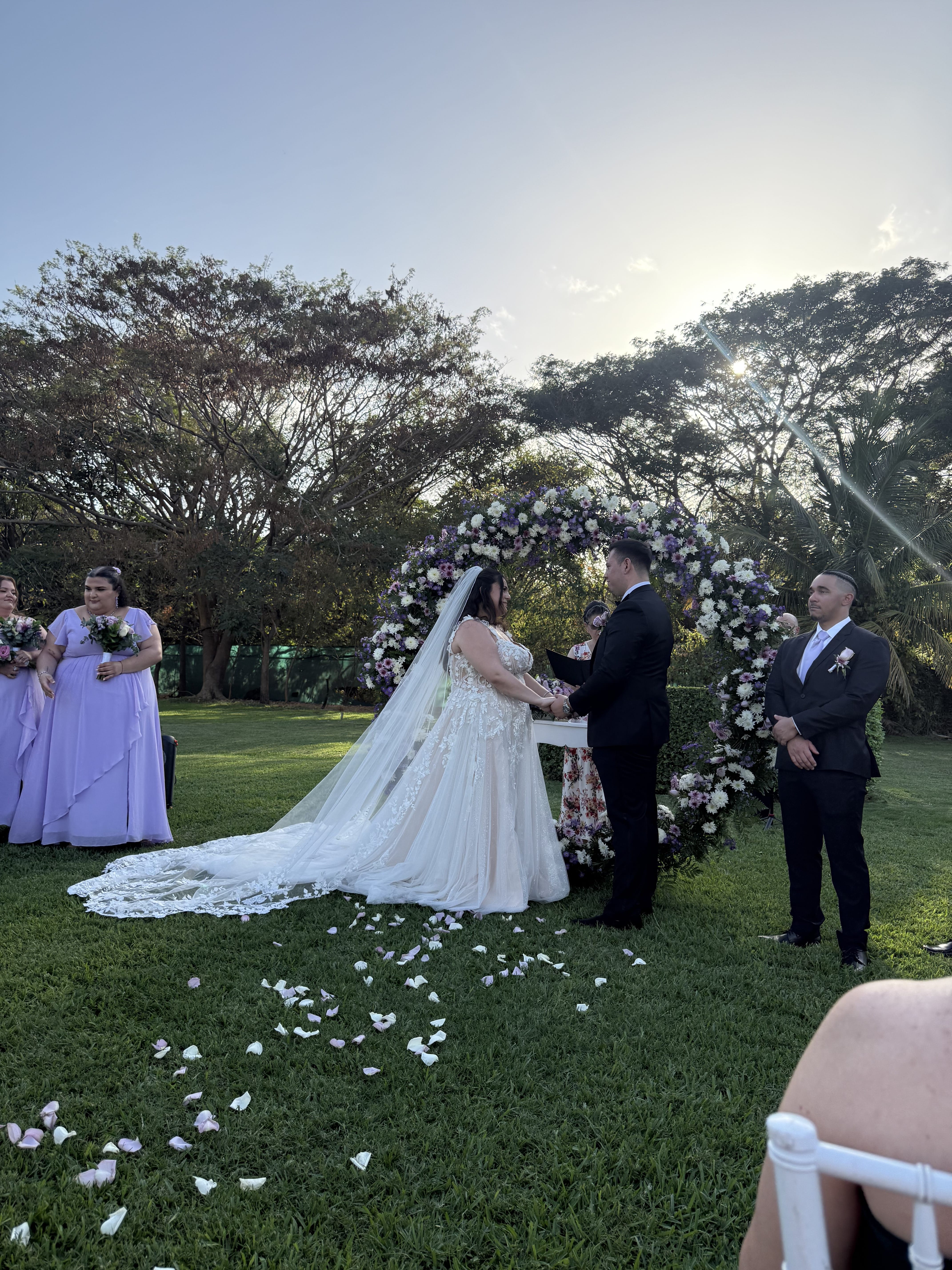 Ashley and Zach exchange wedding vows outdoors before a floral arch, with attendants nearby.