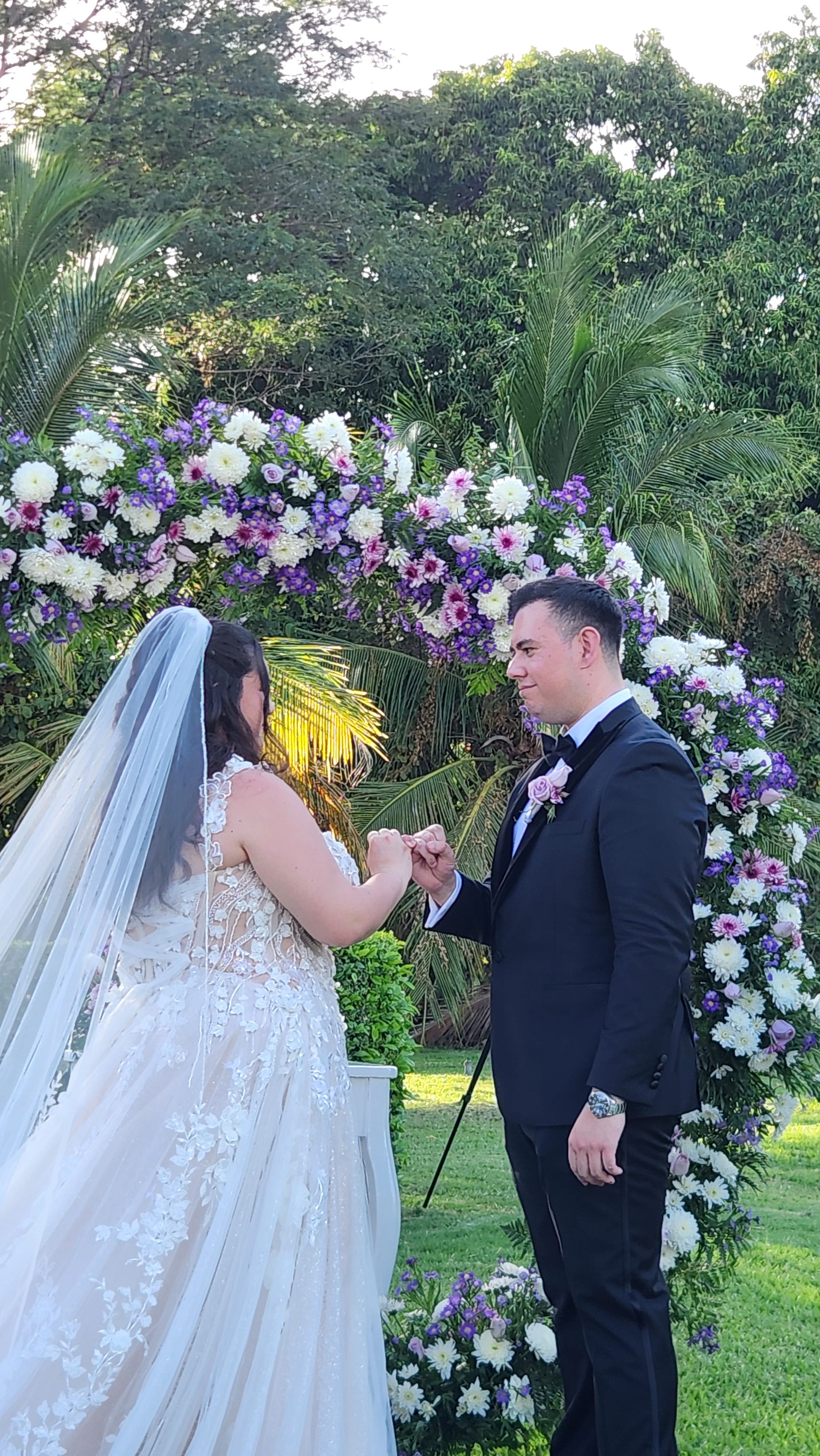 Ashley and Zach share wedding vows outside, standing before a beautiful floral arch at their destination wedding.