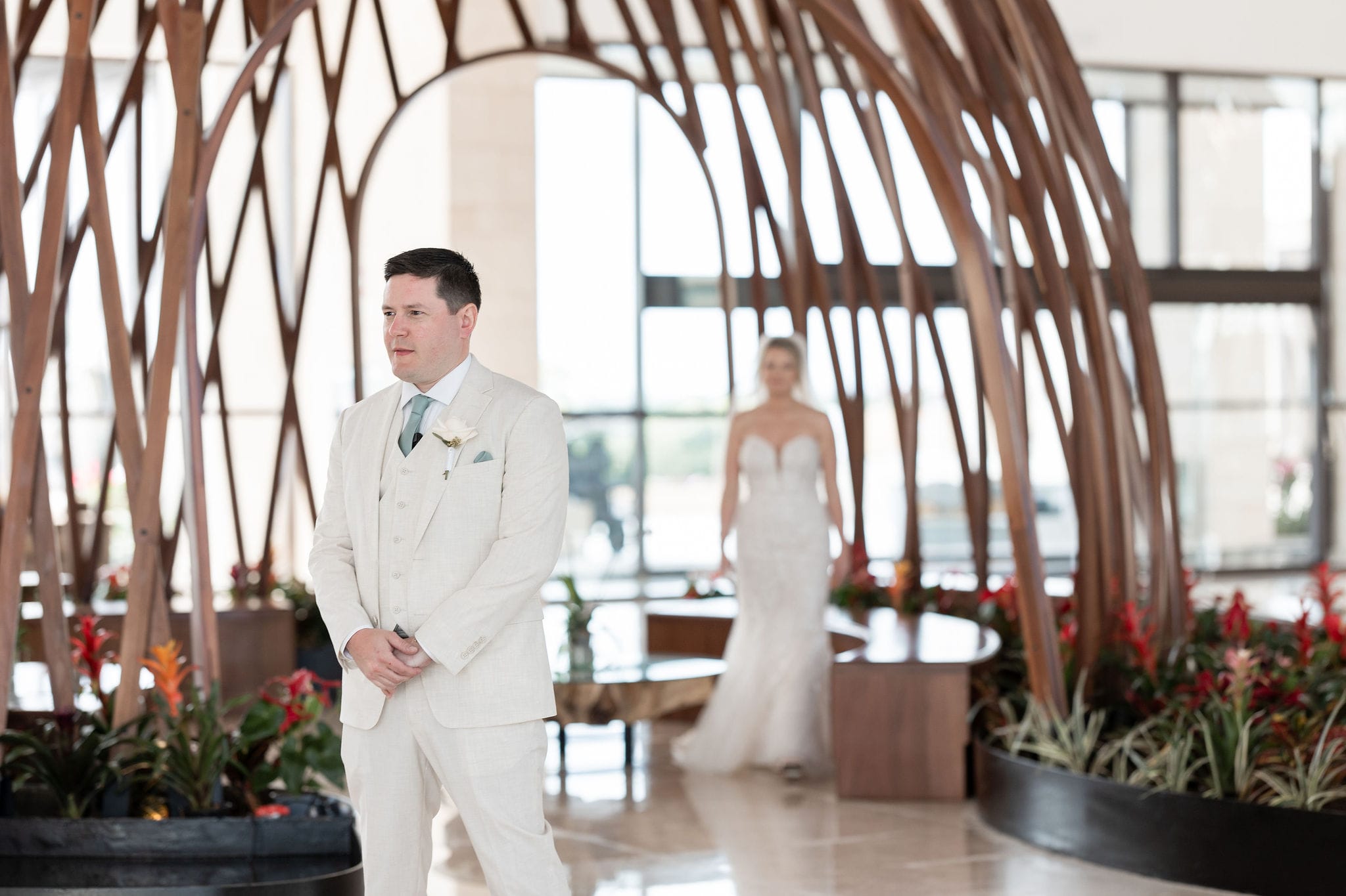 At their destination wedding, a groom in a light suit awaits as his bride in white approaches from behind.