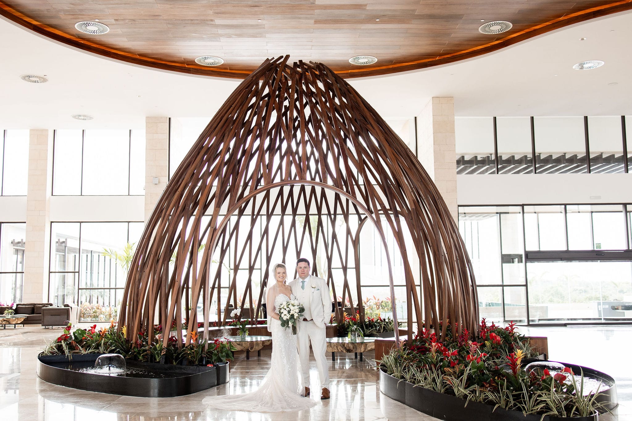 Lauren and Ben pose under a large wooden dome in a modern indoor space at their destination wedding.