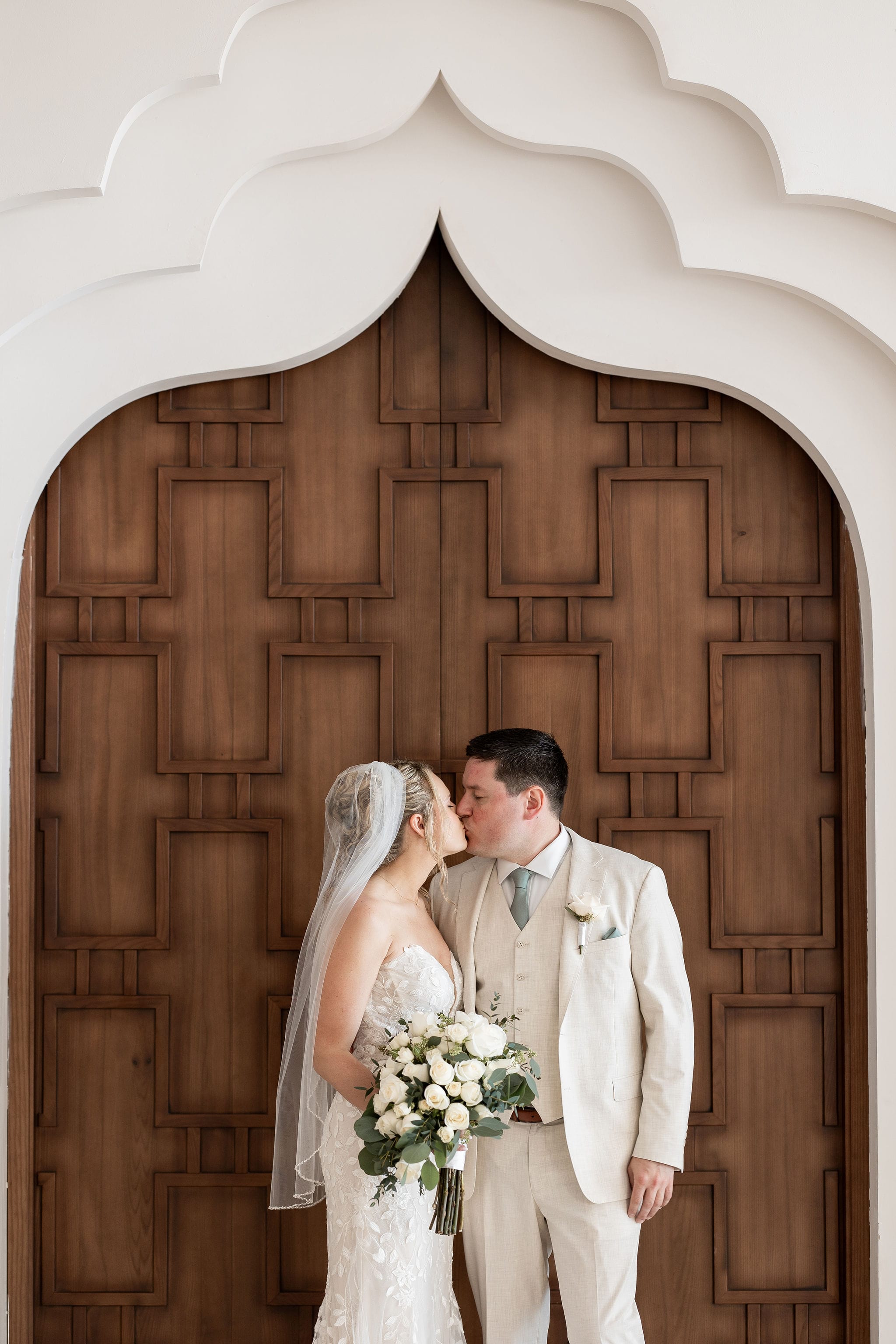 Lauren and Ben face each other at their destination wedding beneath a decorative wooden archway.
