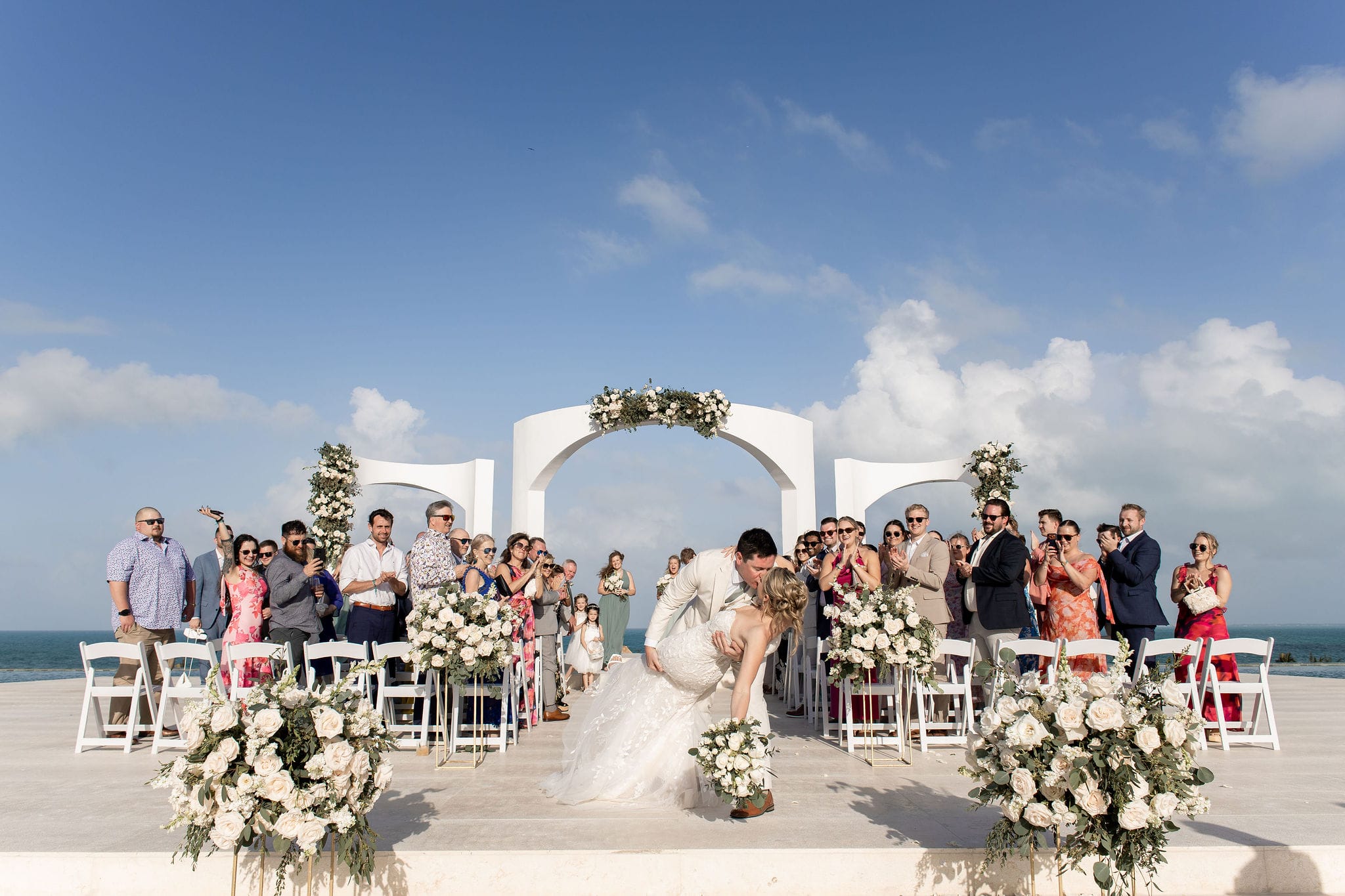 Lauren and Ben kiss at their destination wedding outdoors while guests watch and snap photos.