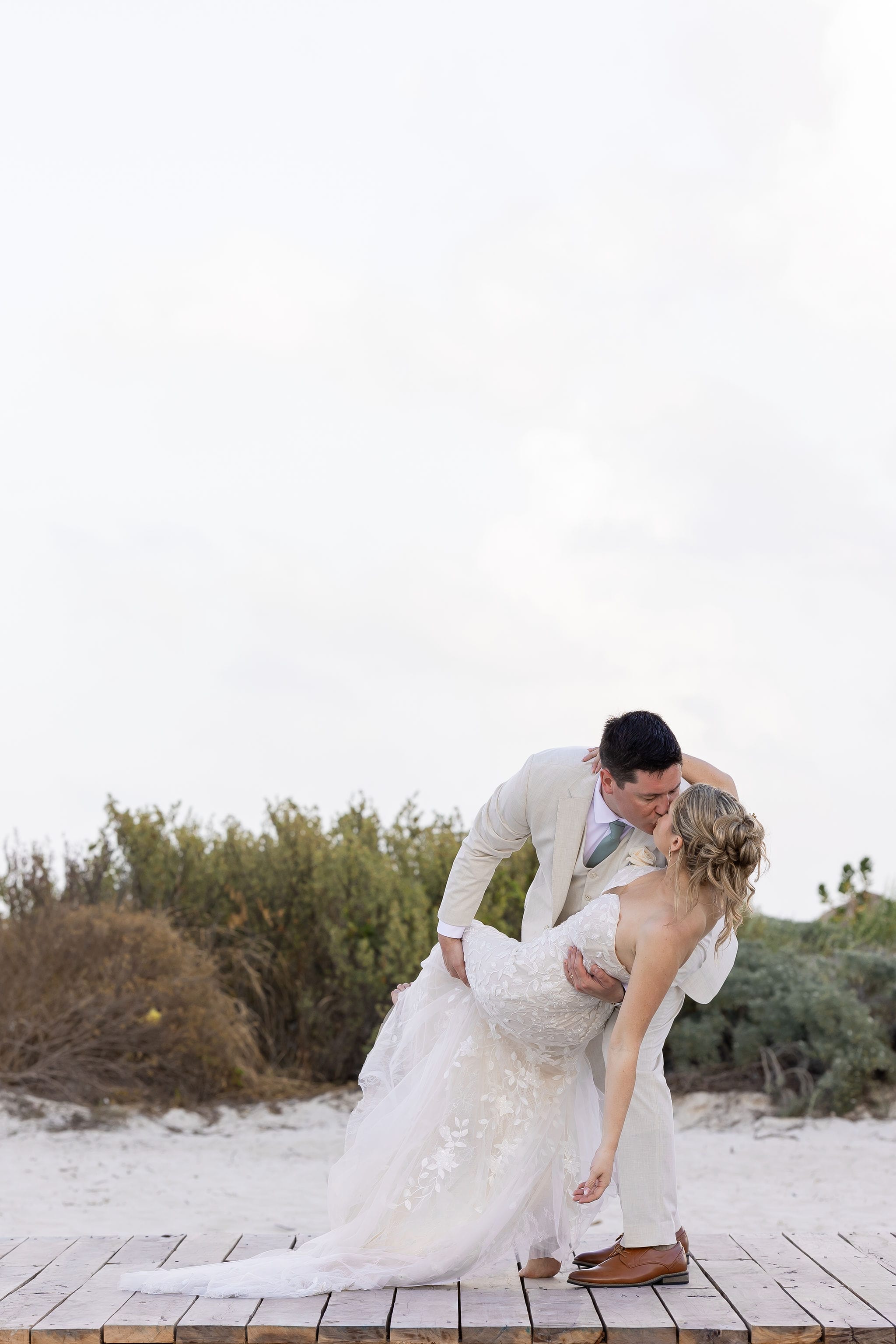 Lauren and Ben share a kiss on a wooden platform outdoors near bushes at their destination wedding.