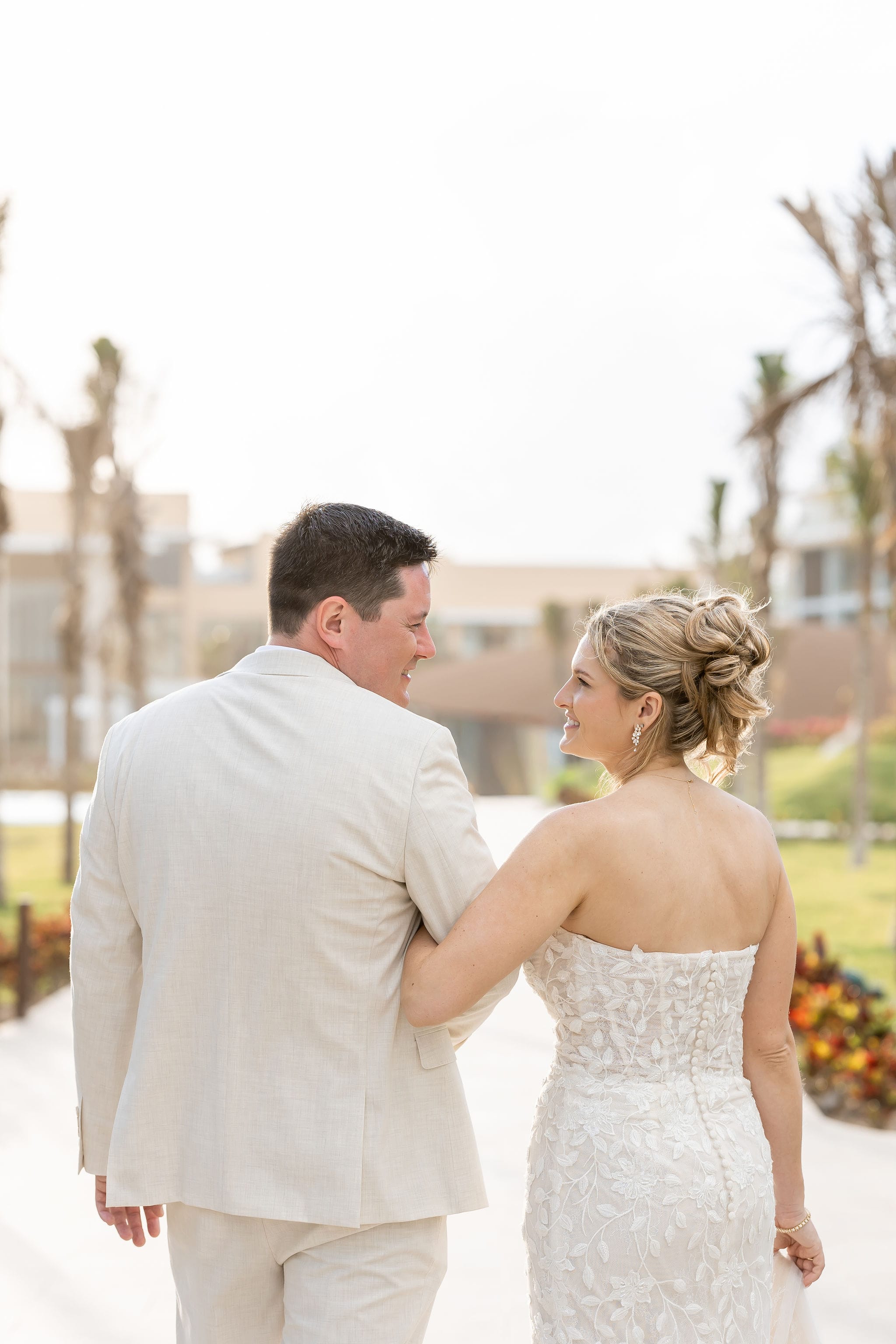 Lauren and Ben walking outdoors, smiling at each other on a sunny day during their destination wedding.