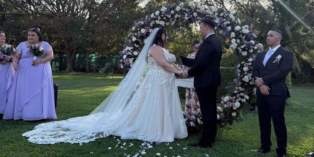 Ashley and Zach hold hands at their destination wedding outdoors, surrounded by bridesmaids and groomsman.
