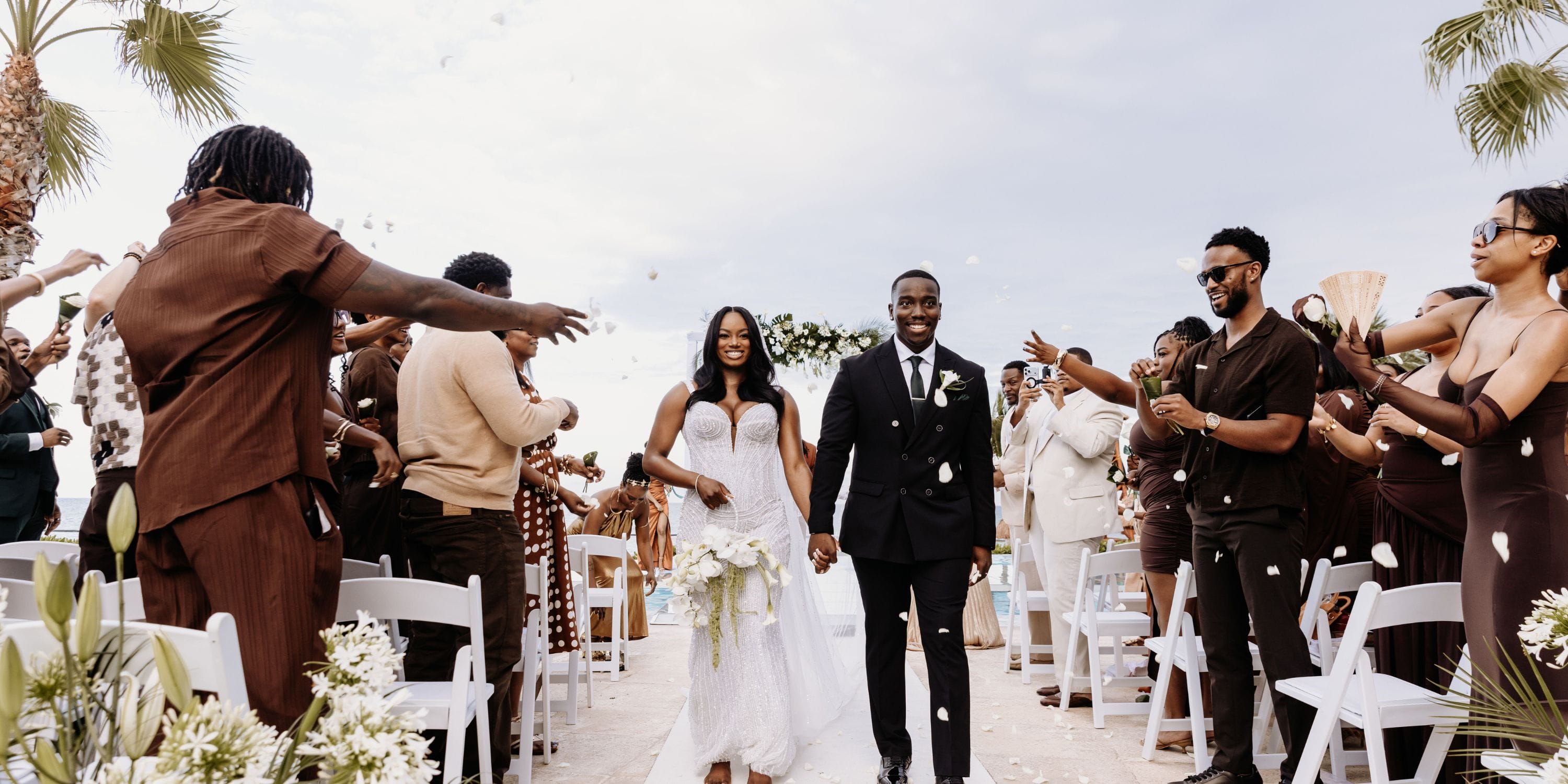 Quishona and Delon walk down the wedding aisle as guests celebrate and toss flower petals.