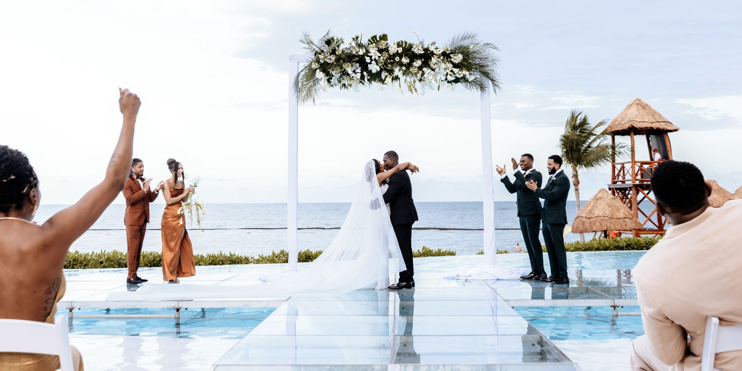 Quishona and Delon kiss at their destination wedding by the sea as applauding guests look on.