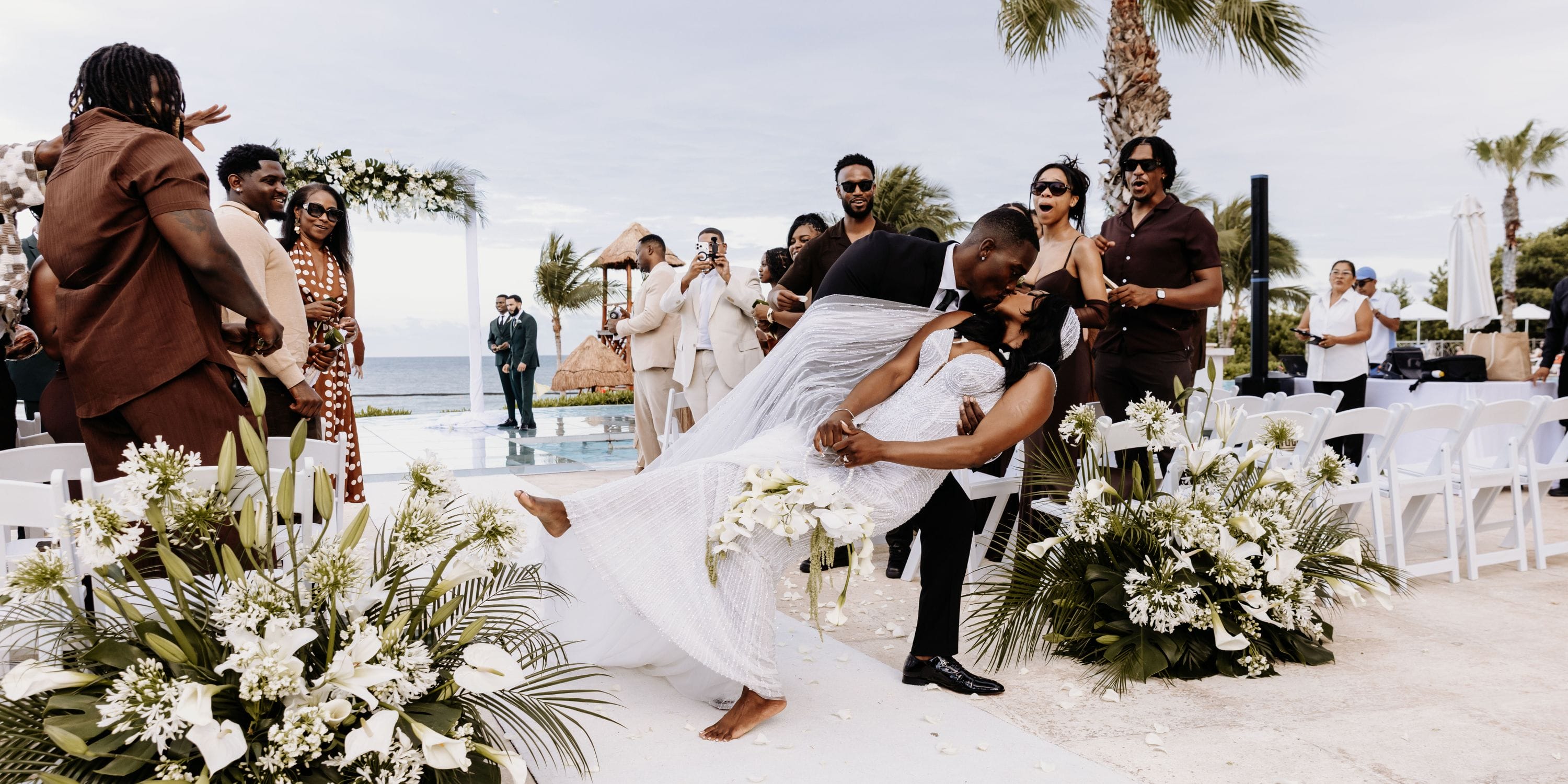 Quishona and Delon share a dip at their picturesque destination wedding by the ocean as guests watch.
