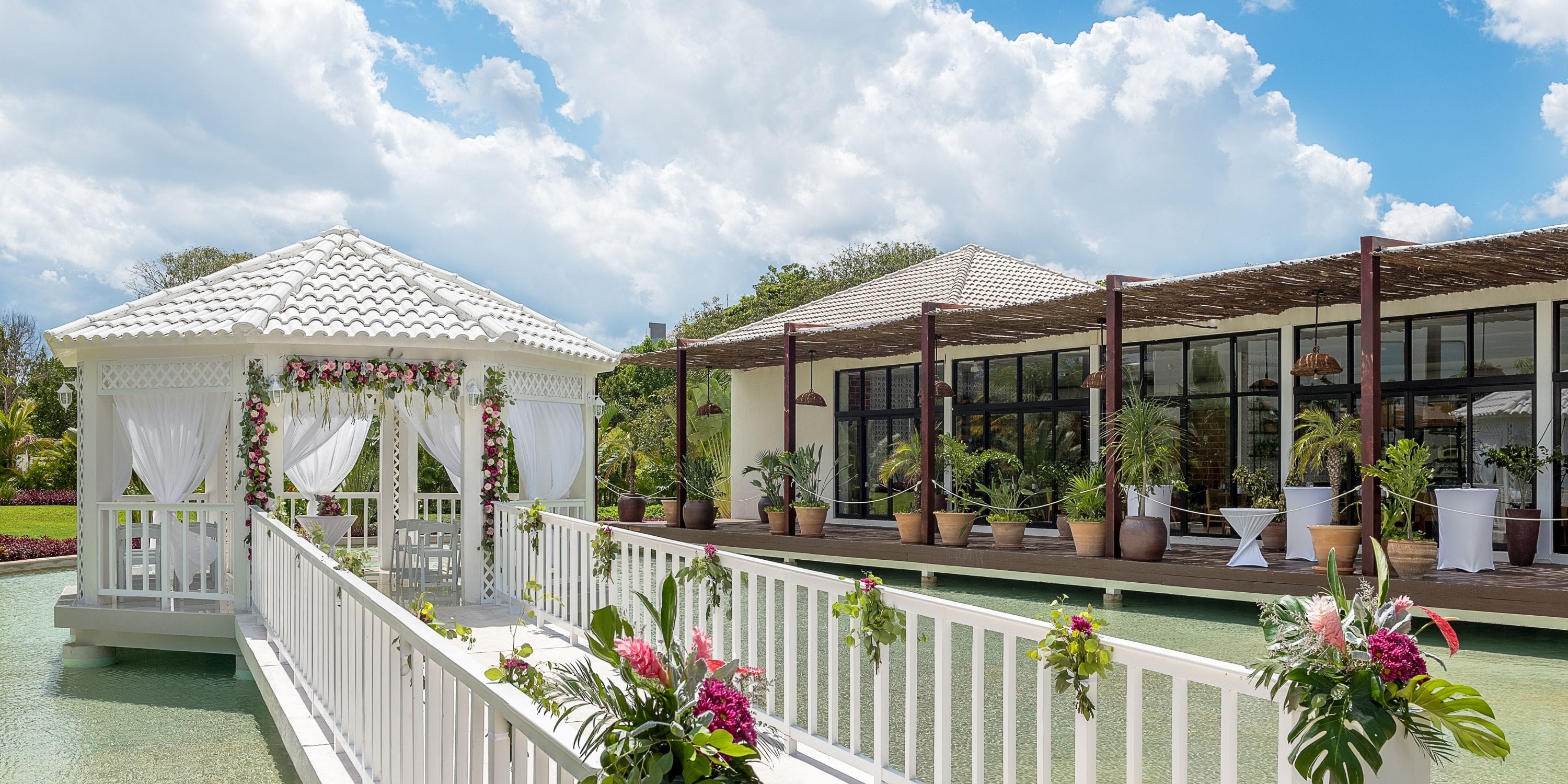White gazebo with wedding flowers on a bridge over water, perfect for a destination wedding setting.