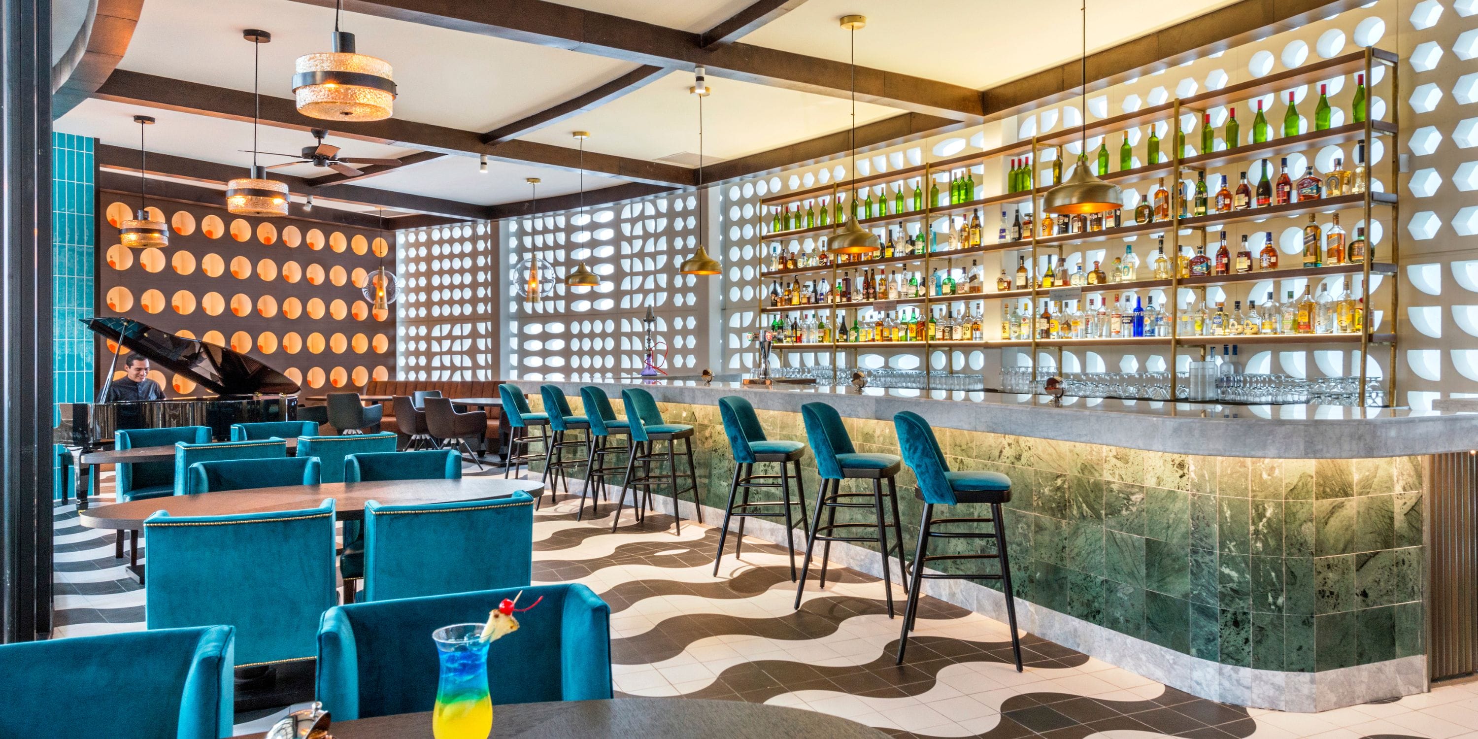 Ocean Riviera Paradise bar for a destination wedding: teal chairs, patterned floor, bottle wall, piano.