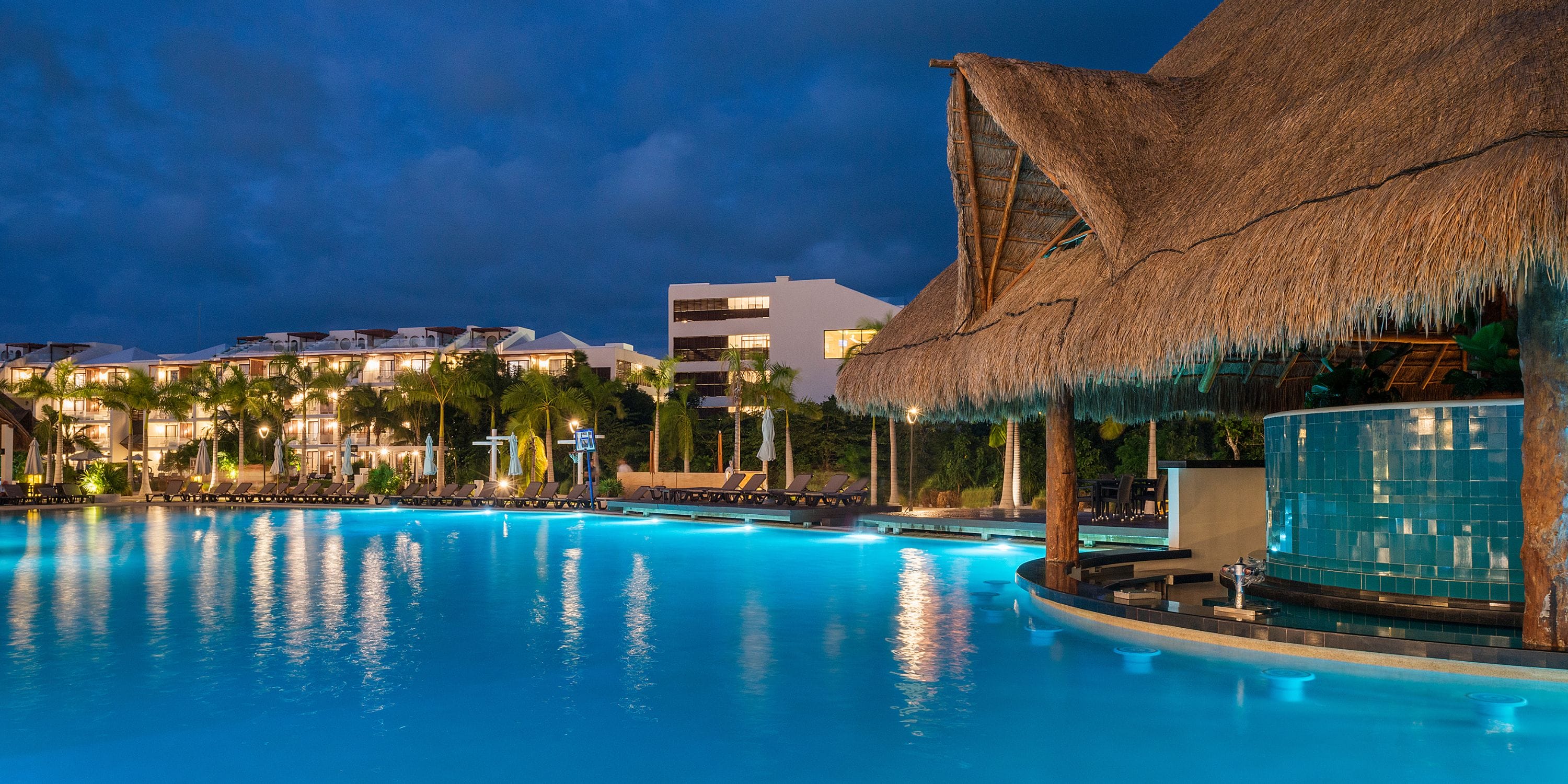 Ocean Riviera Paradise pool at night, perfect for a destination wedding, with thatched-roof bar and lit buildings.