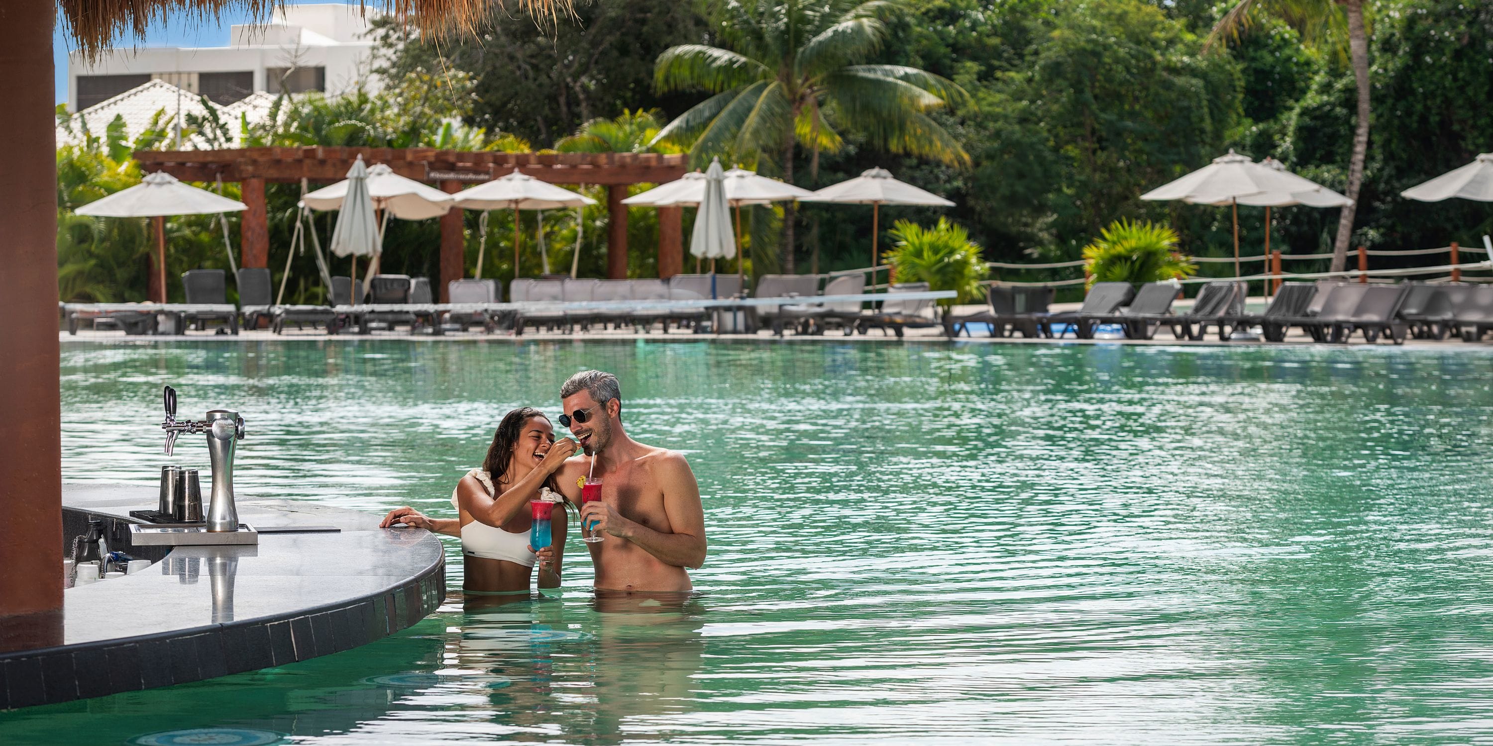 Guests toast drinks at Ocean Riviera Paradise's swim-up bar during a destination wedding, loungers behind.