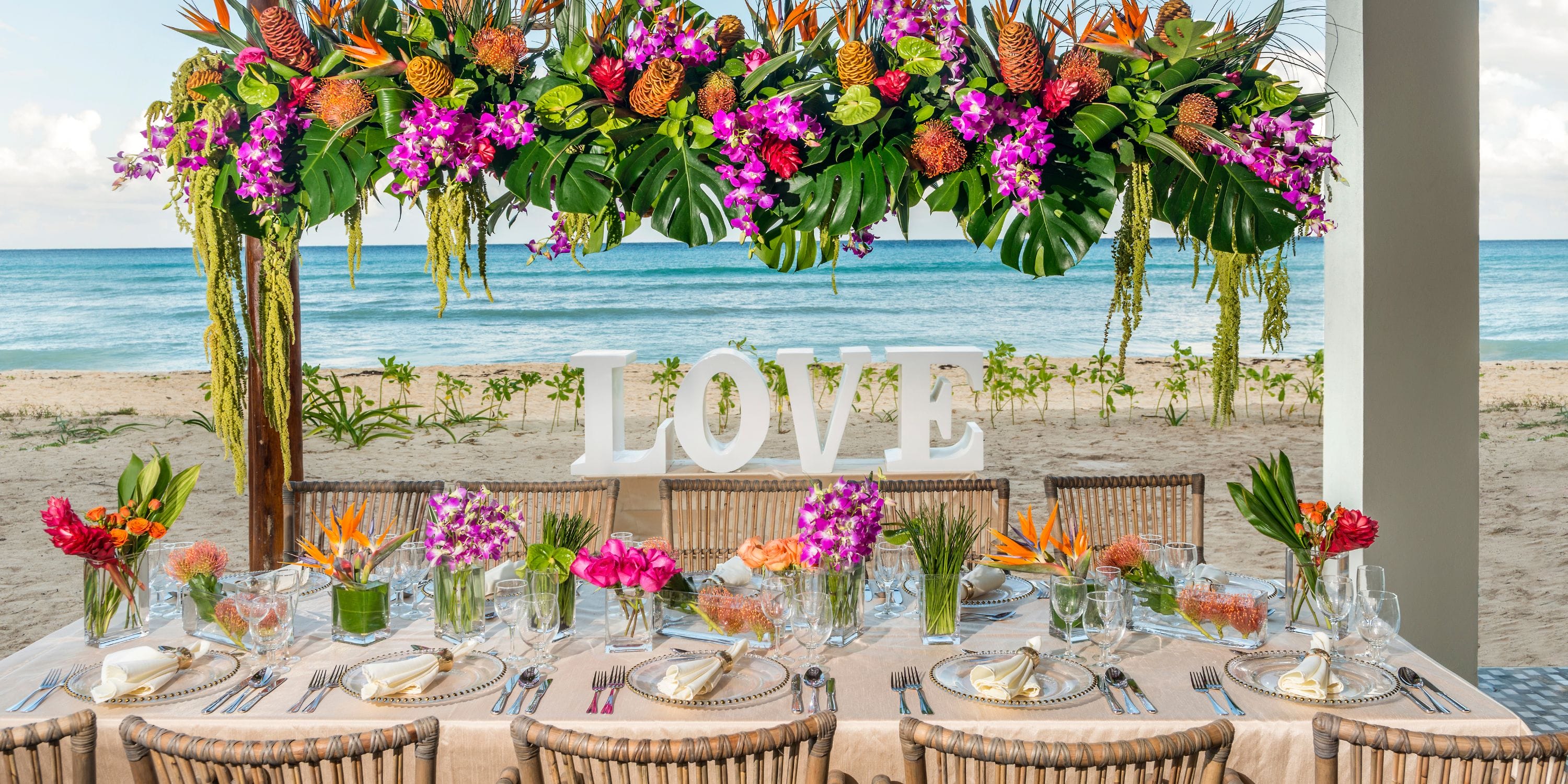 Wedding event table at Ocean Riviera Paradise with flowers and a large "LOVE" sign on the beach.