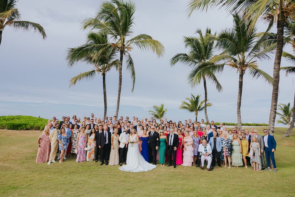 A group poses outdoors at a destination wedding, framed by palm trees in the background.