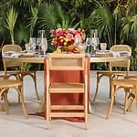 Round outdoor table for six with wooden chairs, floral centerpiece, glassware&mdash;destination wedding.