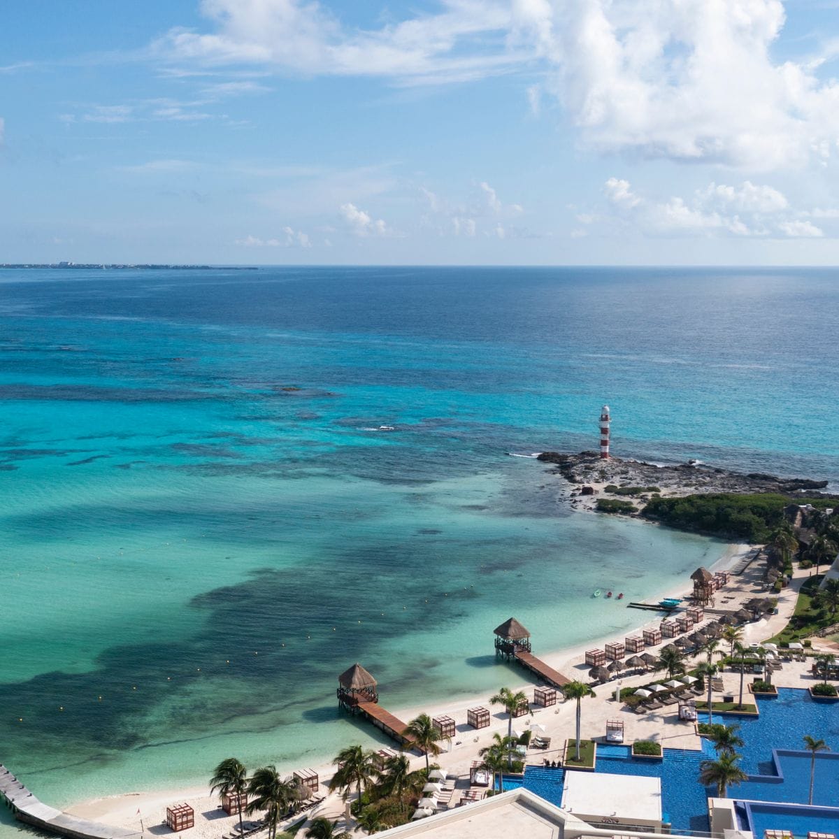 Aerial view of a beach resort with turquoise water, cabanas, and a small lighthouse set for a destination wedding.