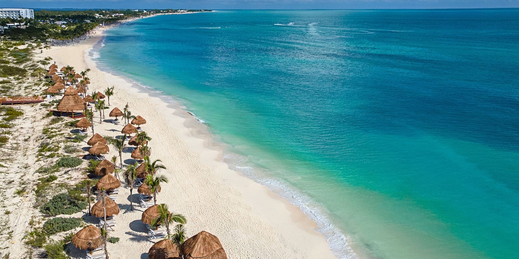 Aerial view of a sandy beach with turquoise water and thatched umbrellas, perfect for a destination wedding.