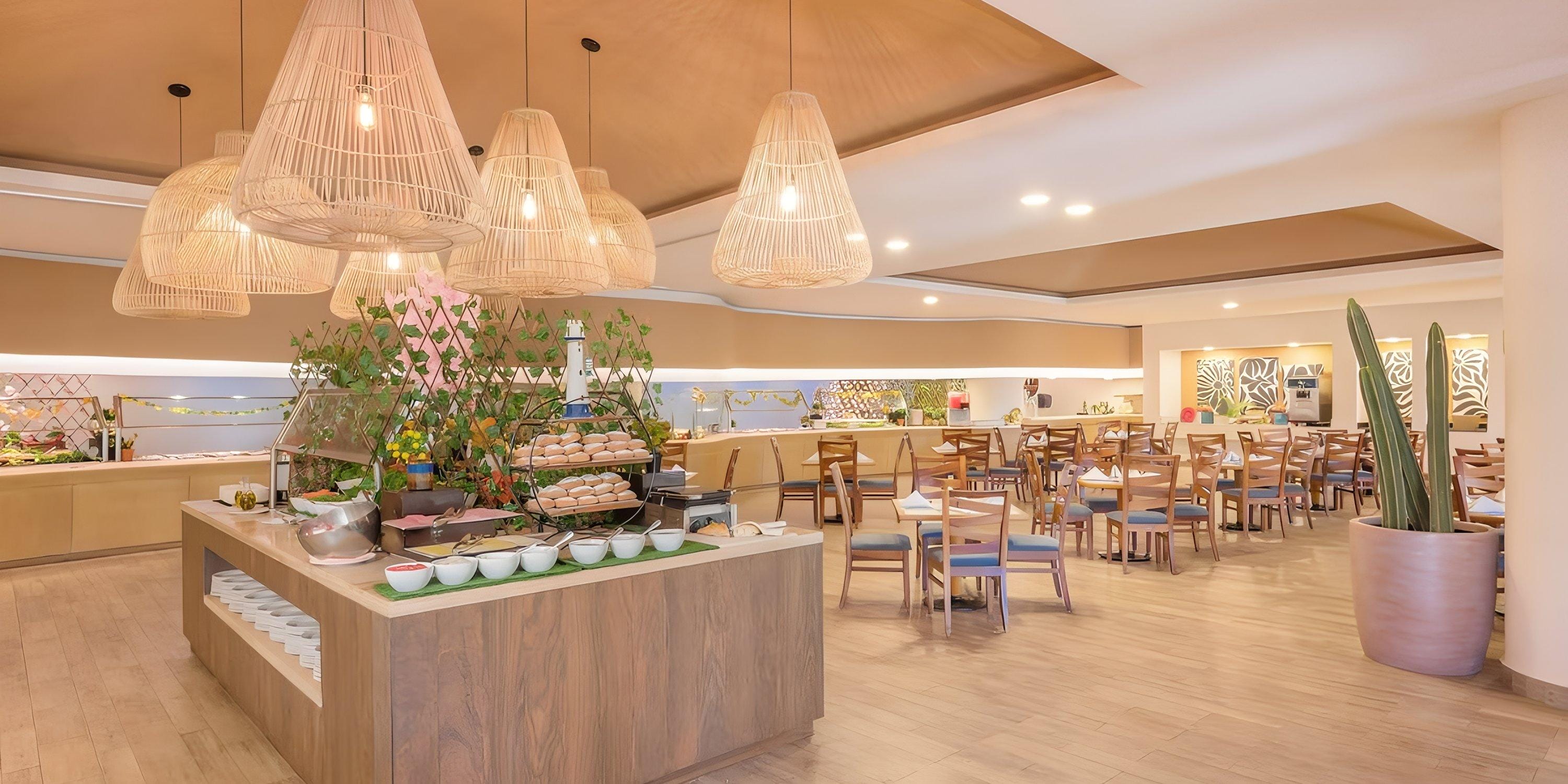 Barcel&oacute; Grand Faro Los Cabos offers a modern buffet, perfect for destination weddings, with wood tables and chairs under stylish hanging lights.